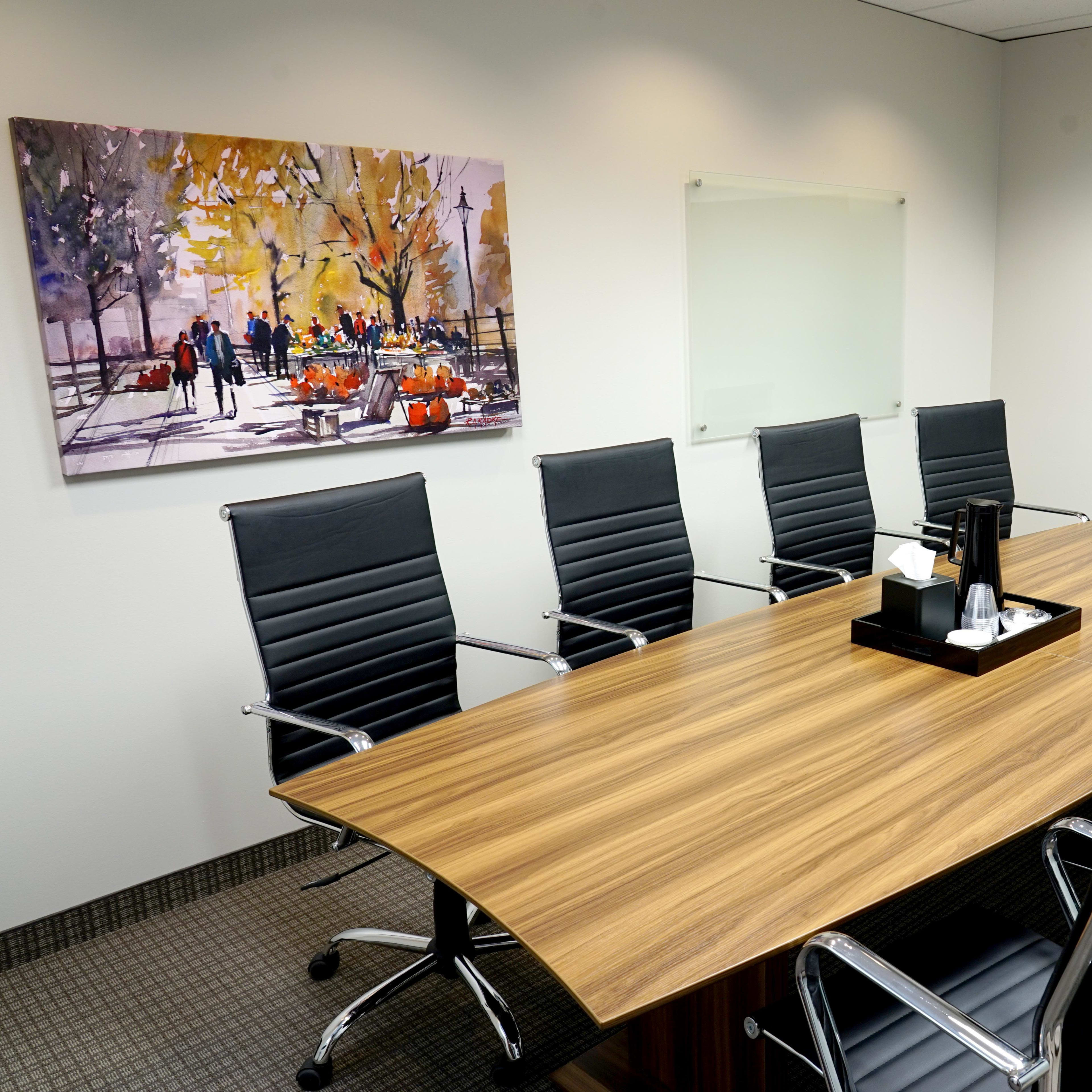 A modern conference room features a long wooden table surrounded by six black chairs, a wall-mounted television, and a colorful artwork depicting a park scene.