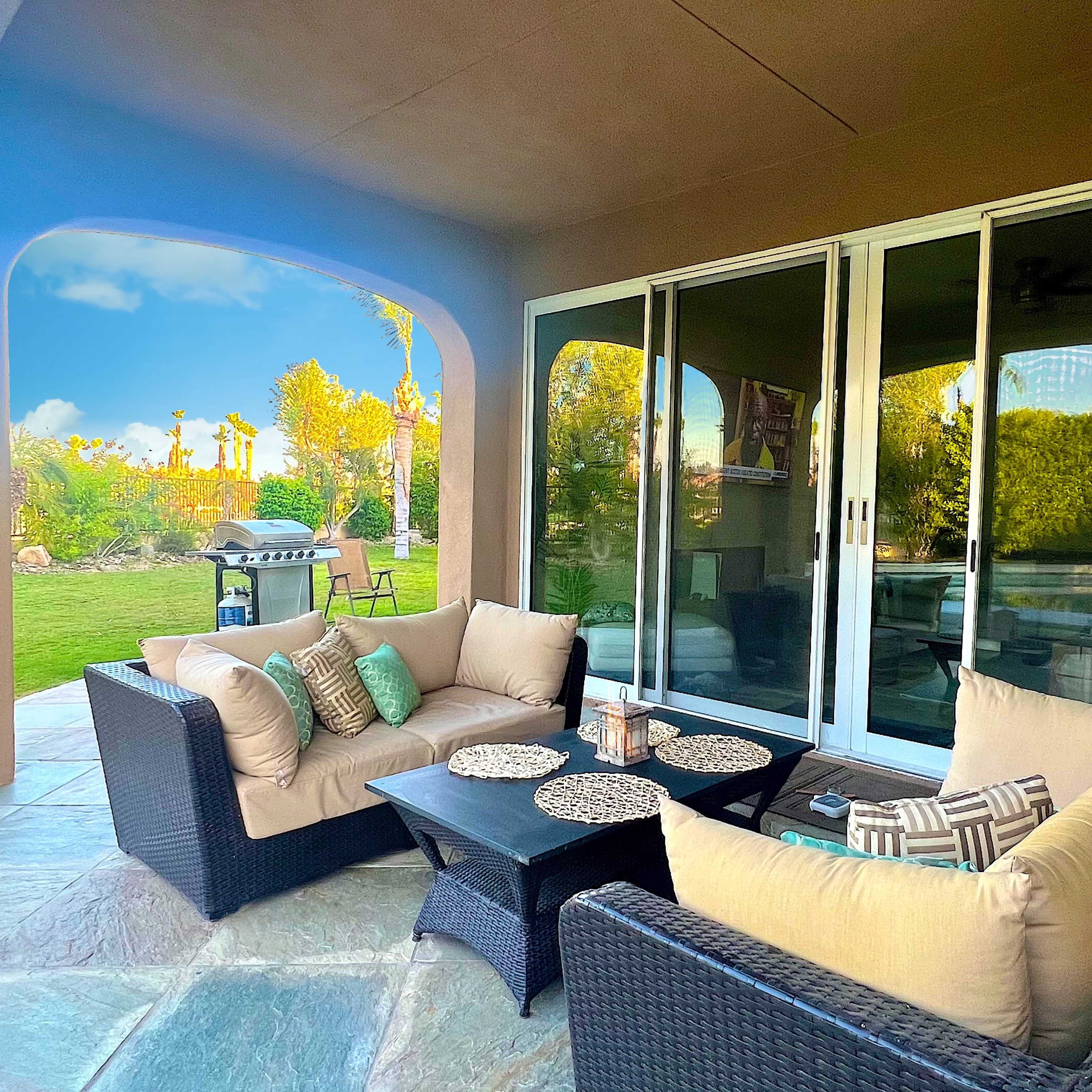 A covered patio with a seating area made of wicker furniture and a view of a landscaped backyard.
