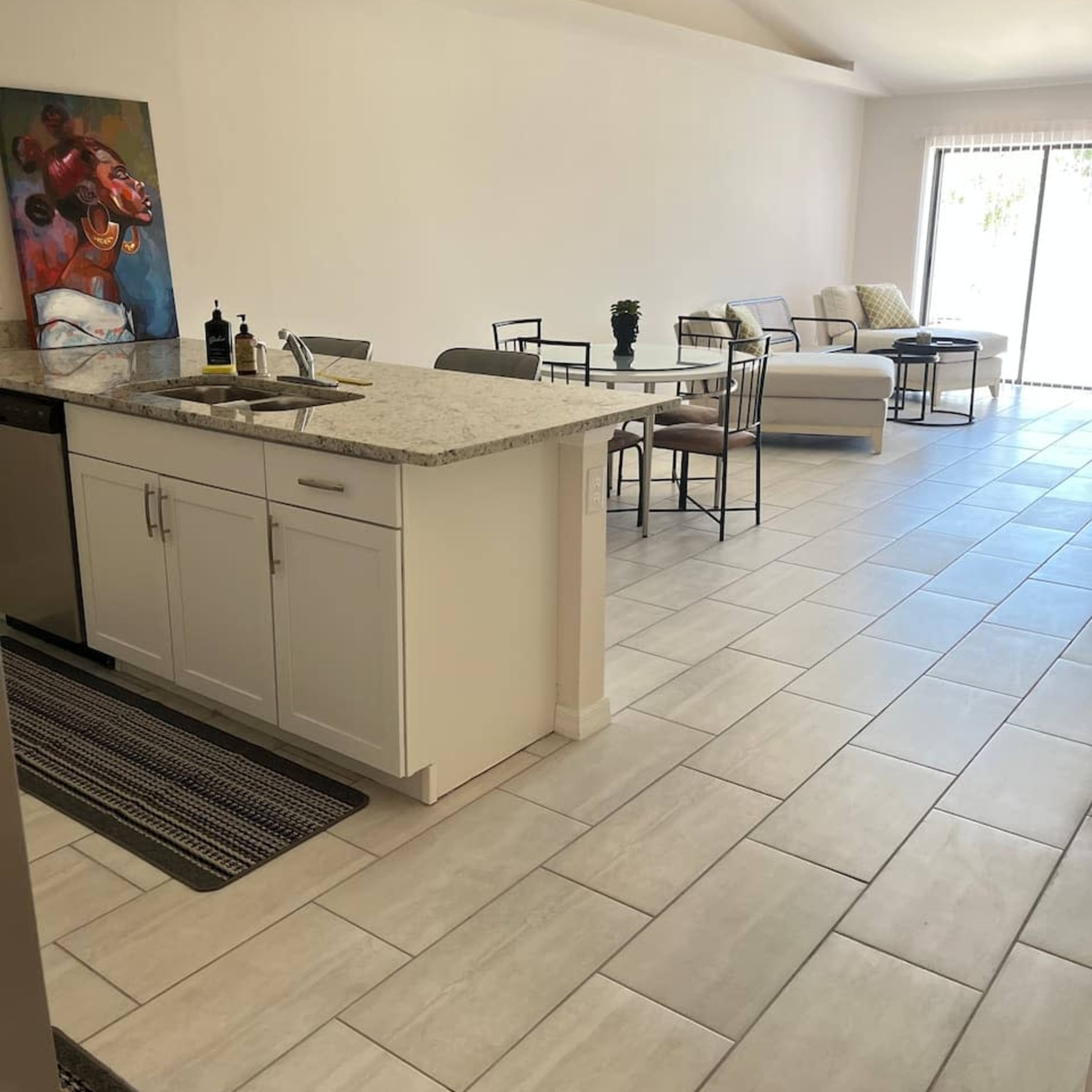 A modern kitchen area with a granite countertop, dining table, and a living space featuring a sofa and large sliding glass door to the outside.