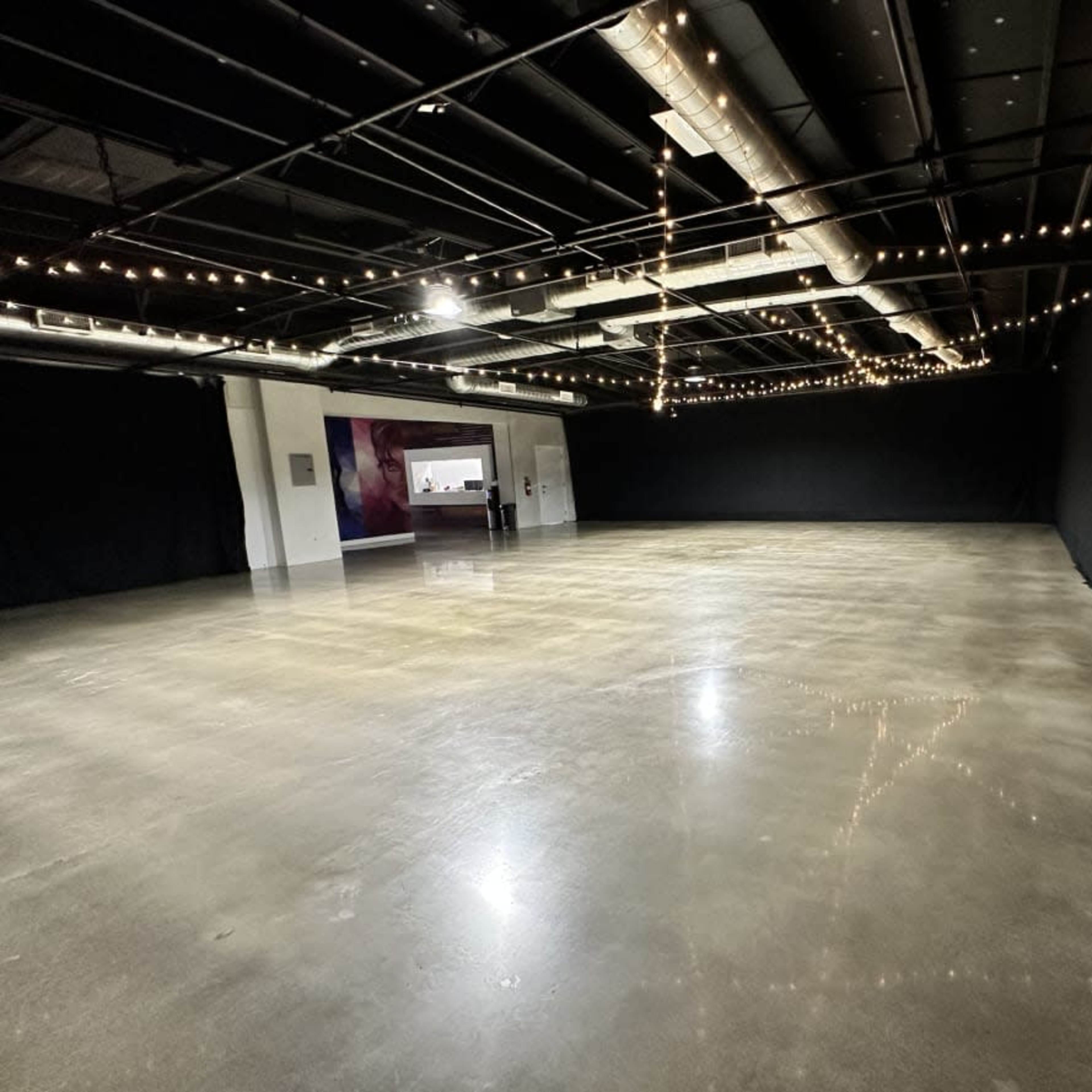 A spacious interior with a polished concrete floor, black curtains lining the walls, and strings of lights hanging from the ceiling.