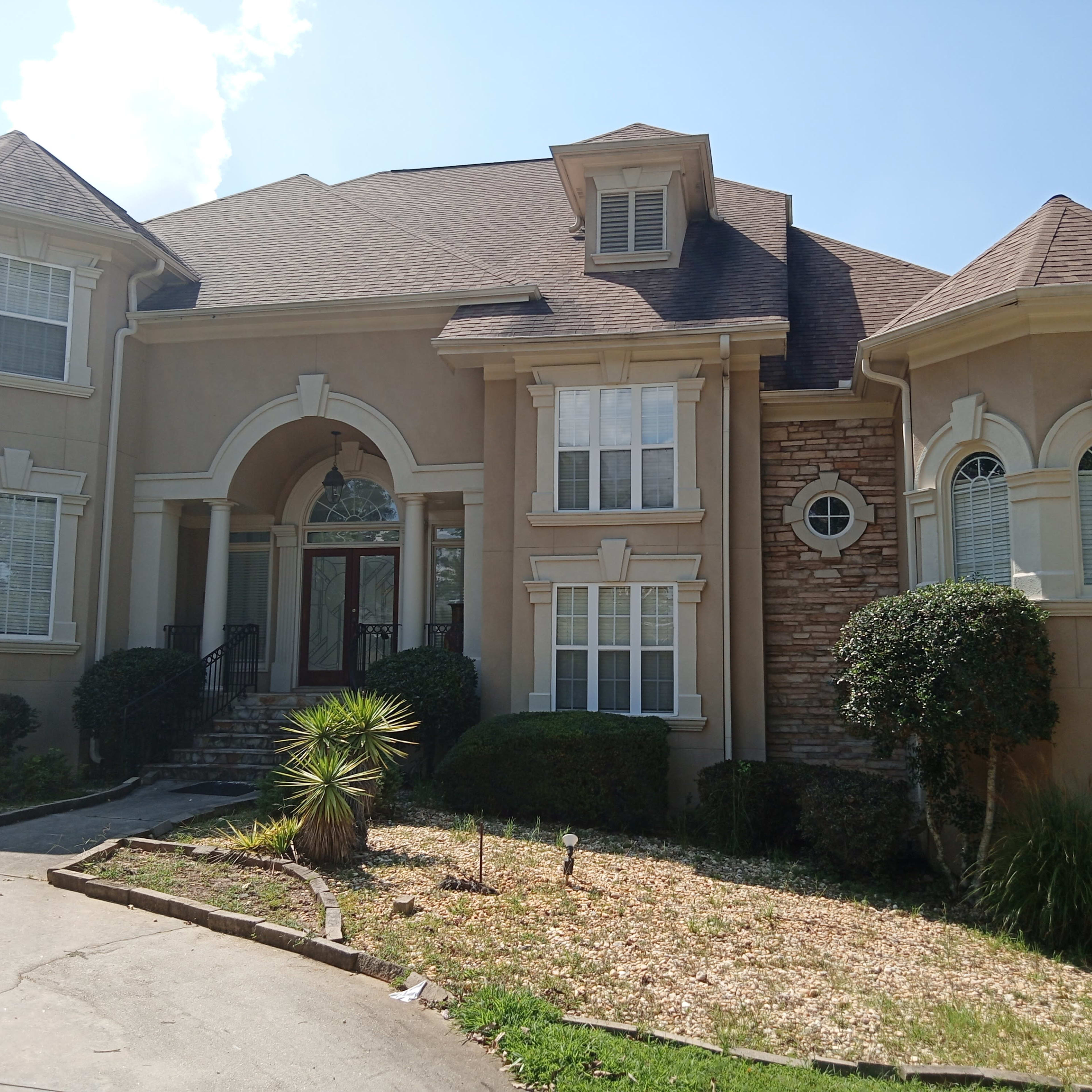 A large, two-story house with a mix of stone and stucco exterior, featuring a prominent entryway and multiple windows.