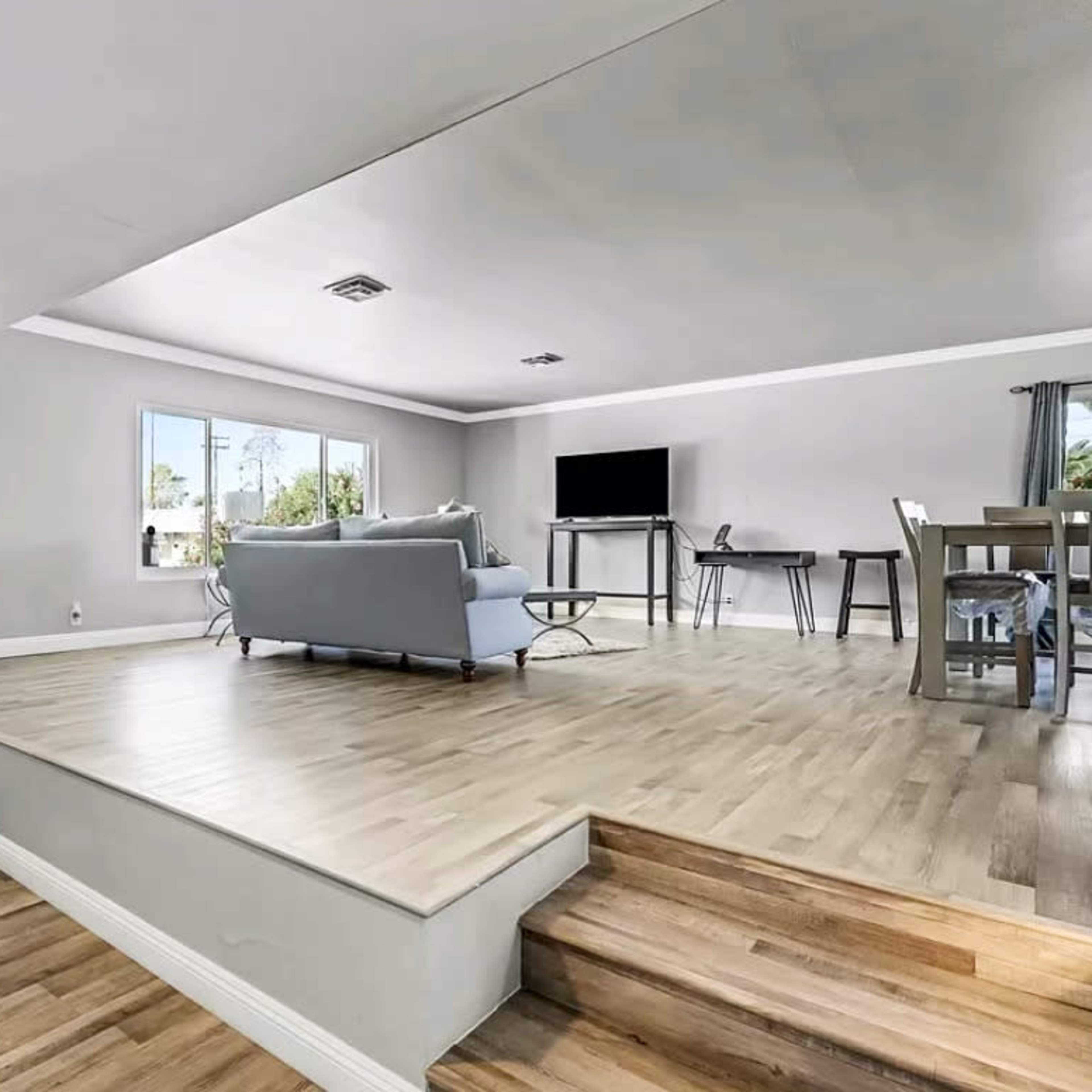 A modern living area with an open floor plan, featuring a light-colored hardwood floor, a seating area, and a dining table.