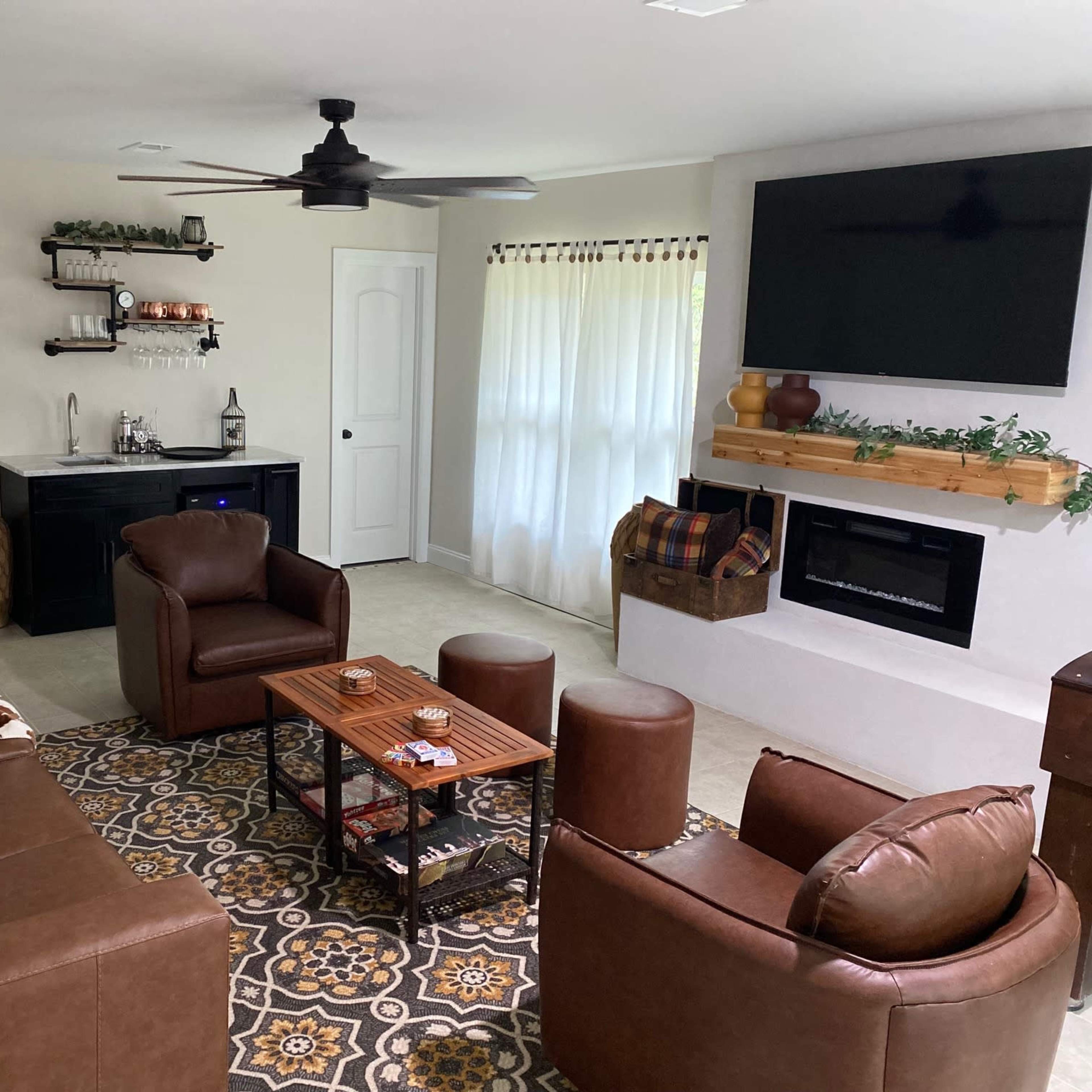 A cozy living room features a leather sectional sofa, two armchairs, a coffee table, and a wall-mounted television above an electric fireplace.
