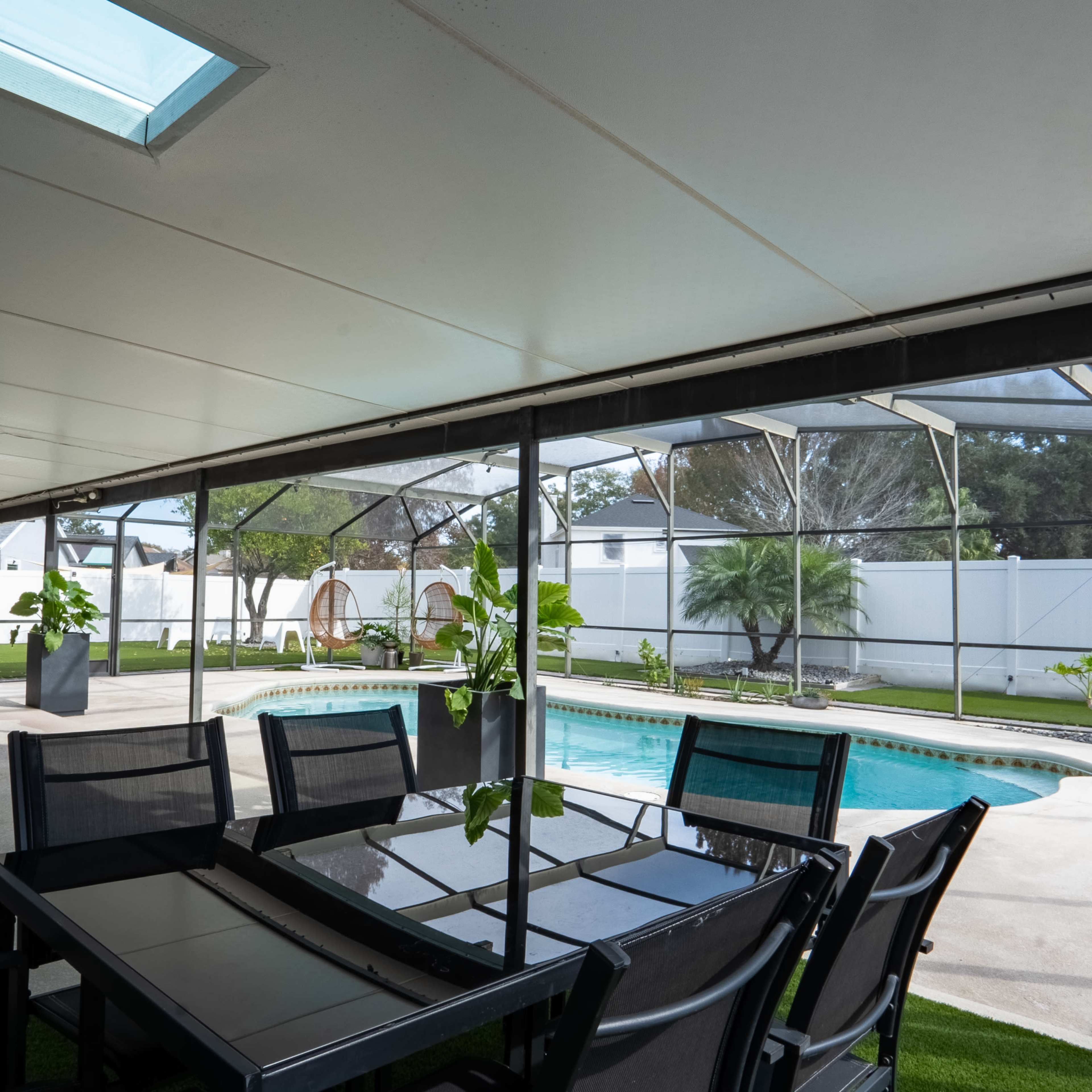 A screened-in patio with a dining table and chairs overlooking a swimming pool surrounded by greenery.