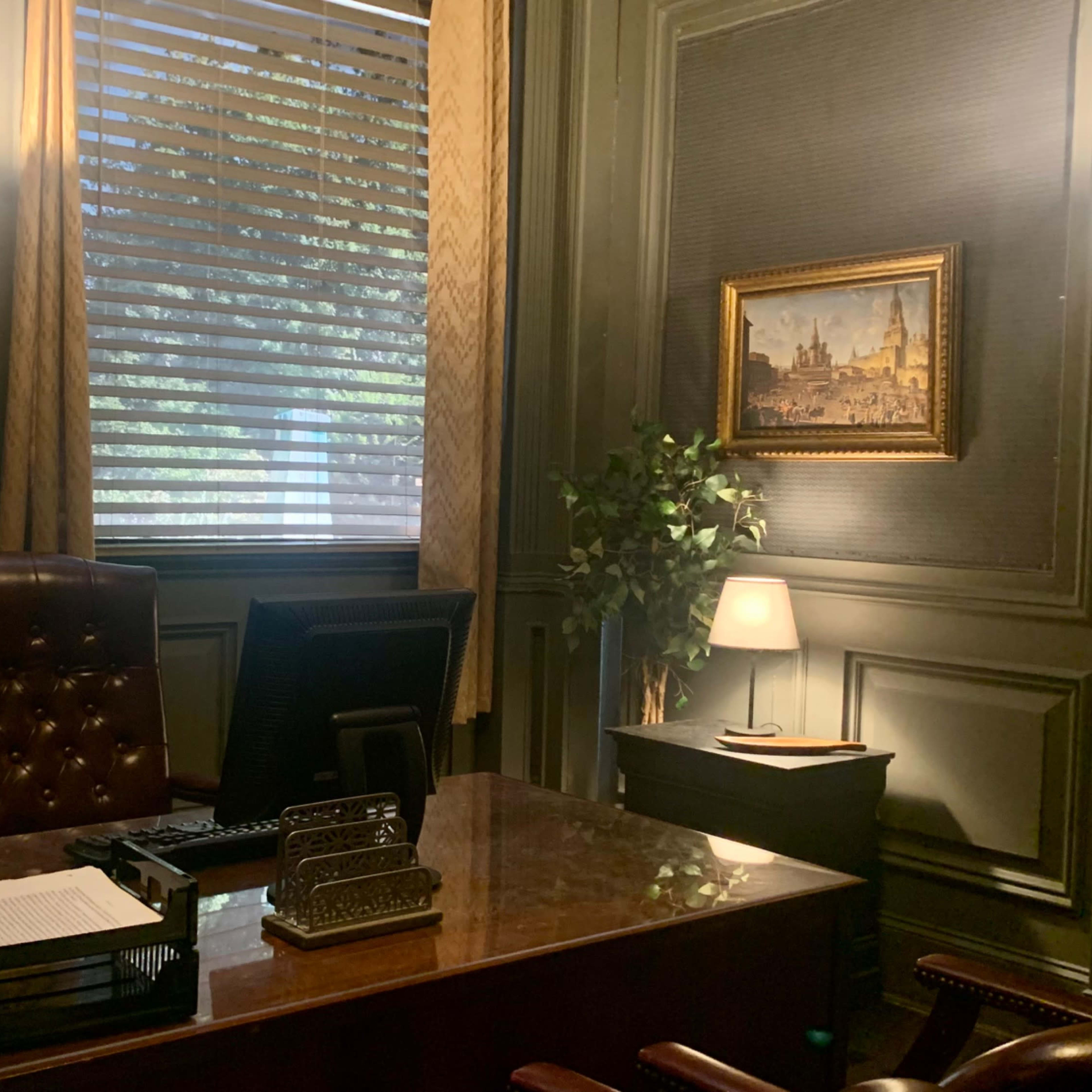 A well-furnished office with a wooden desk, a computer, a chair, and a decorative painting on the wall.