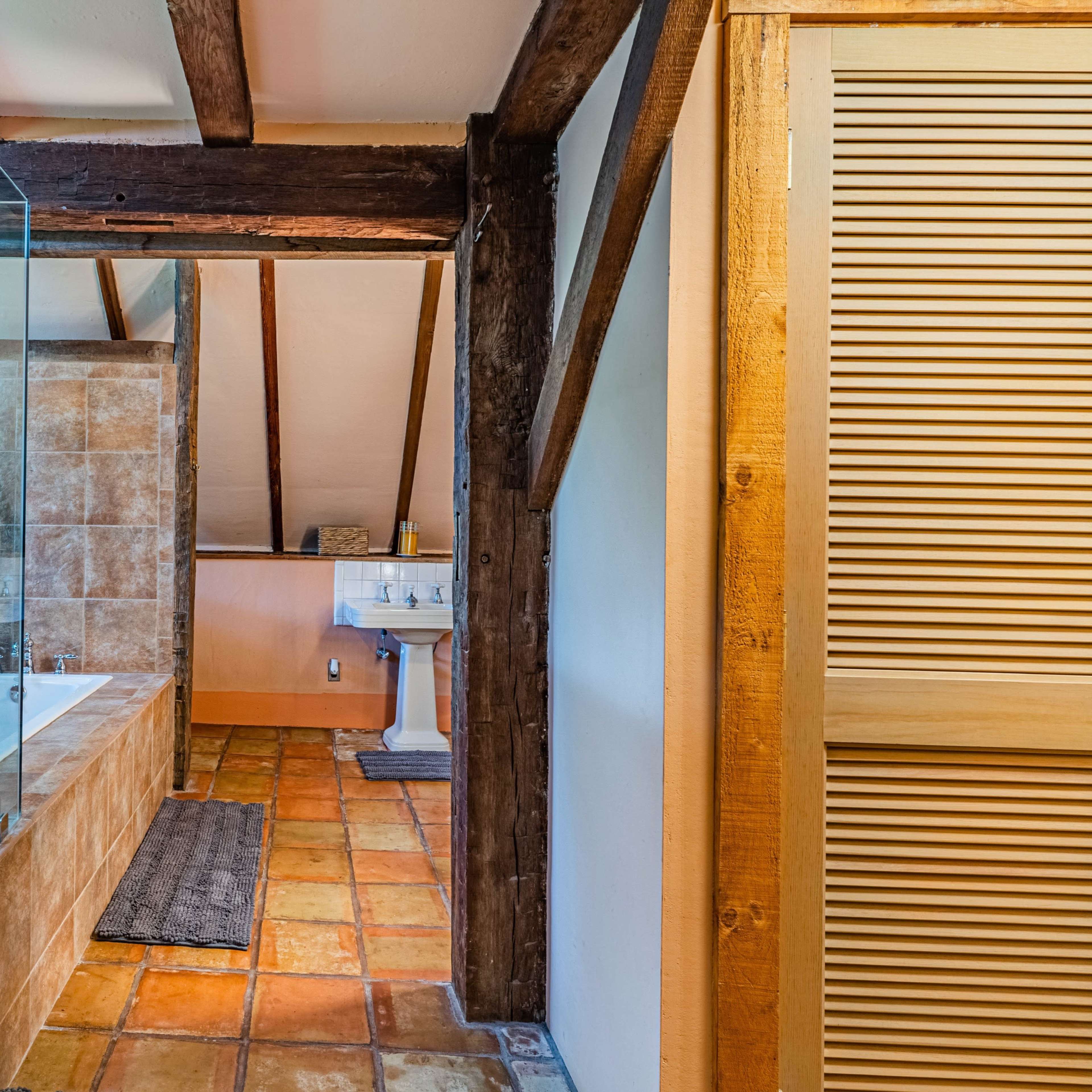 A bathroom featuring a glass shower enclosure, a freestanding bathtub, and wooden beams on the ceiling.