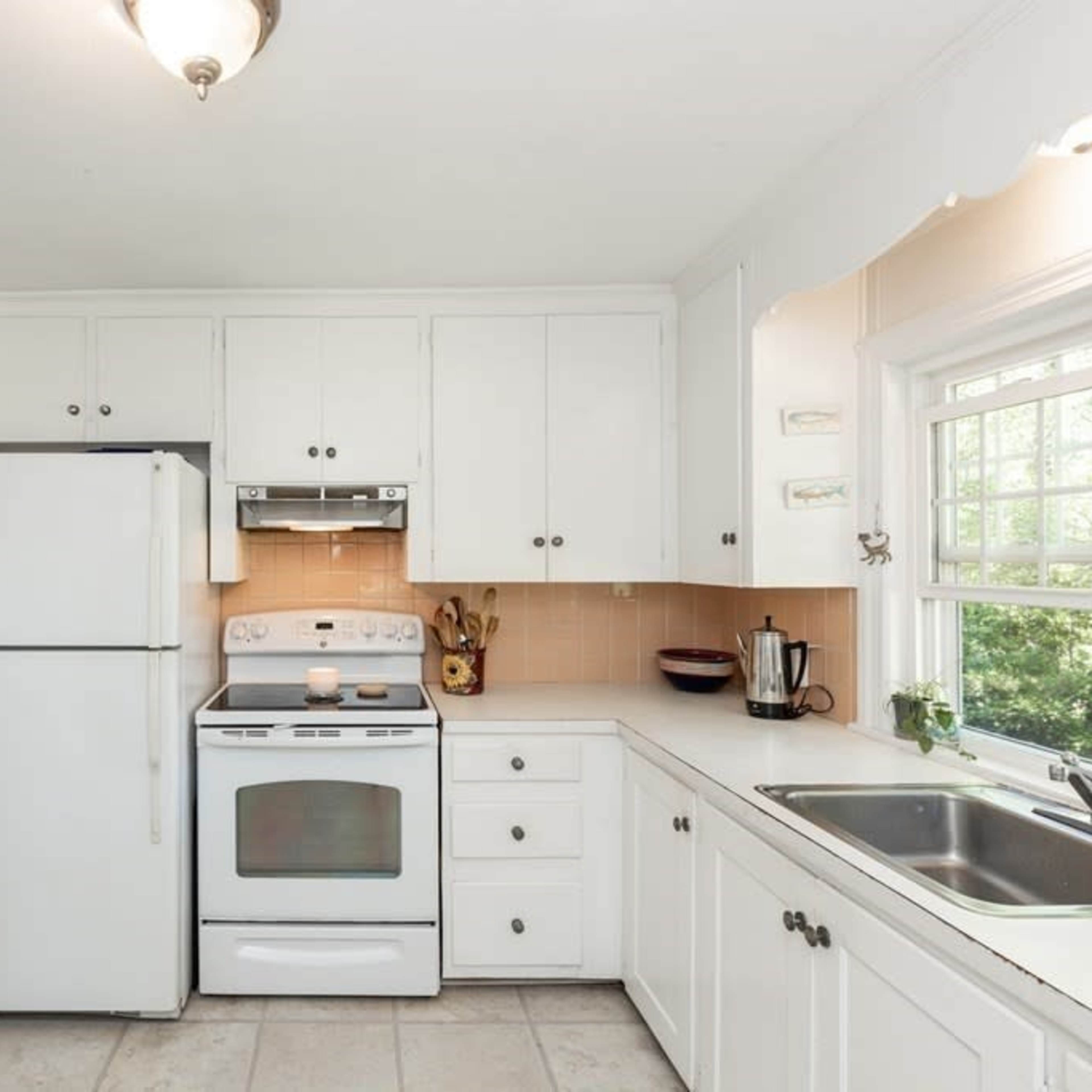A white kitchen featuring a refrigerator, stove, and sink with light-colored countertops and cabinets.