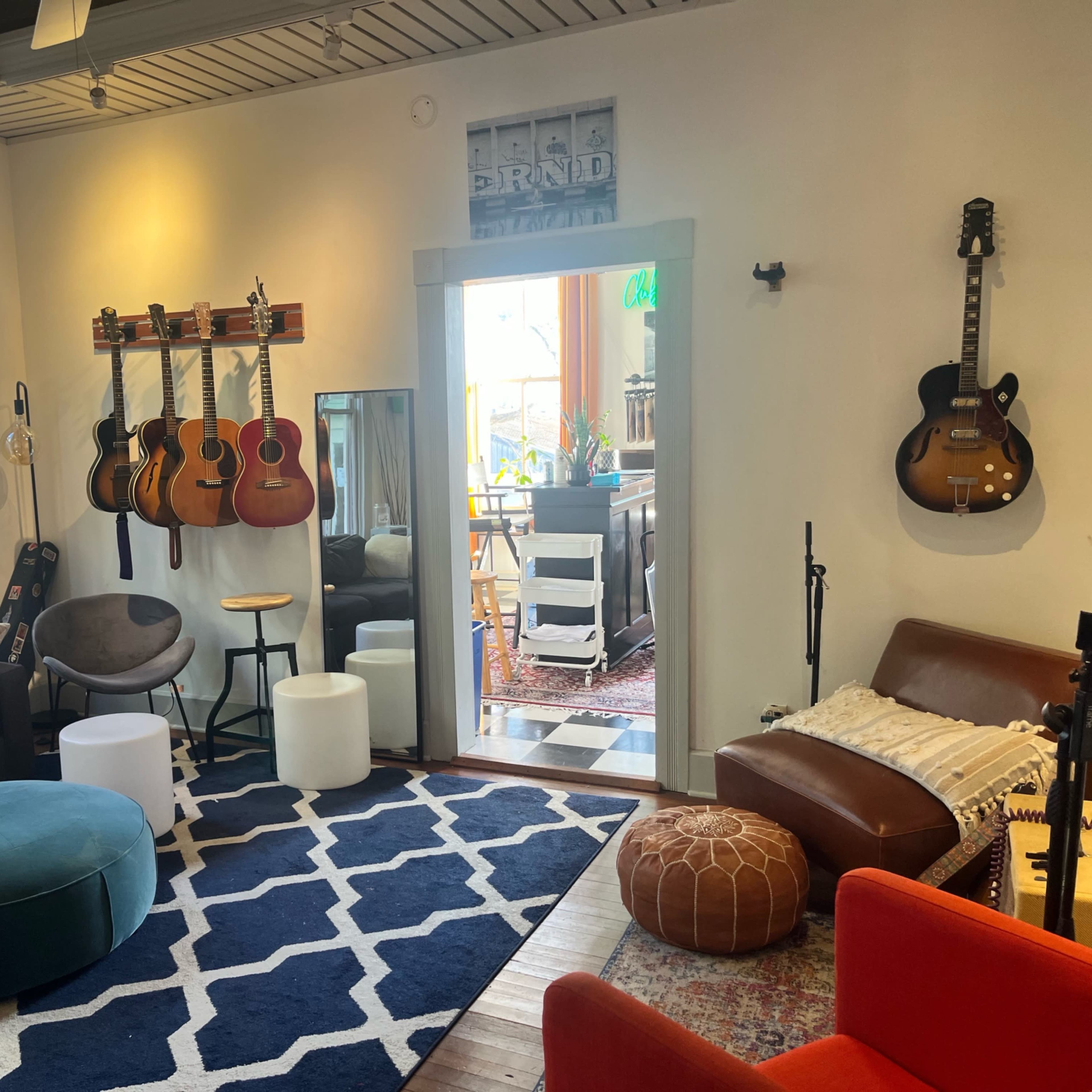 A cozy living room with a mix of seating options, guitars mounted on the wall, and an open doorway leading to a bright outdoor area.