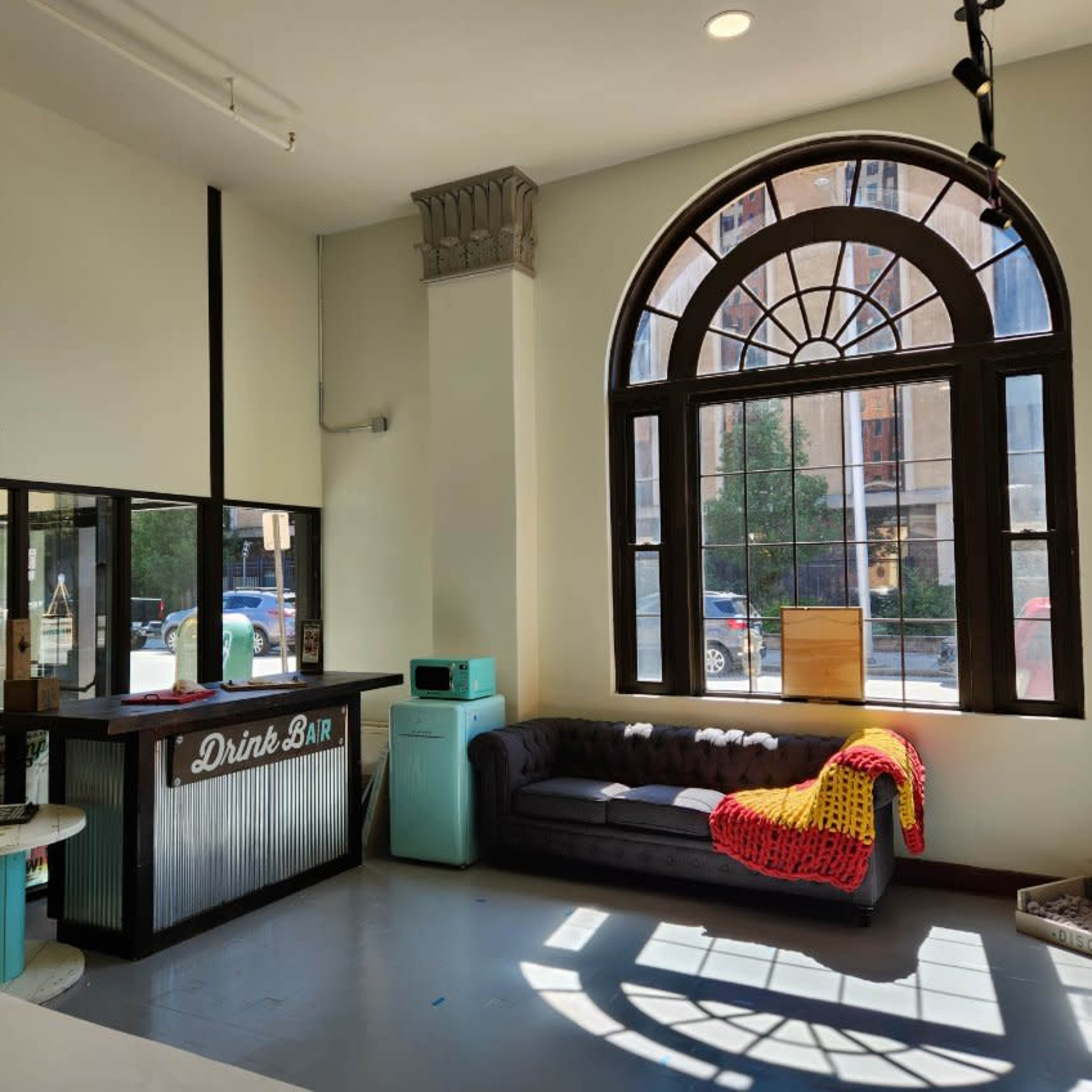 The interior features a drink bar next to a large arched window, with a couch draped in a colorful blanket facing the street.