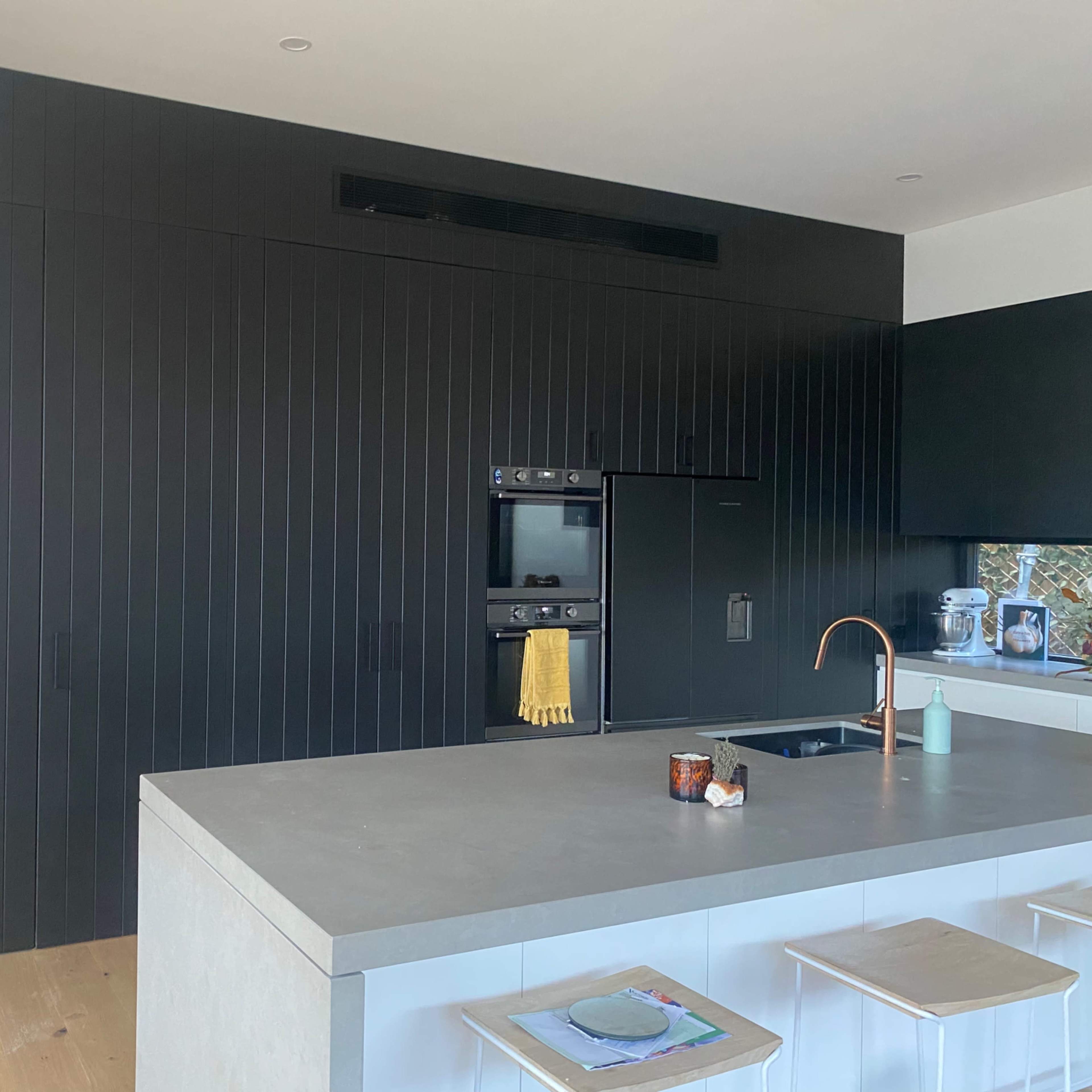 A modern kitchen with a black paneled wall, a gray island counter, and minimalistic stools.