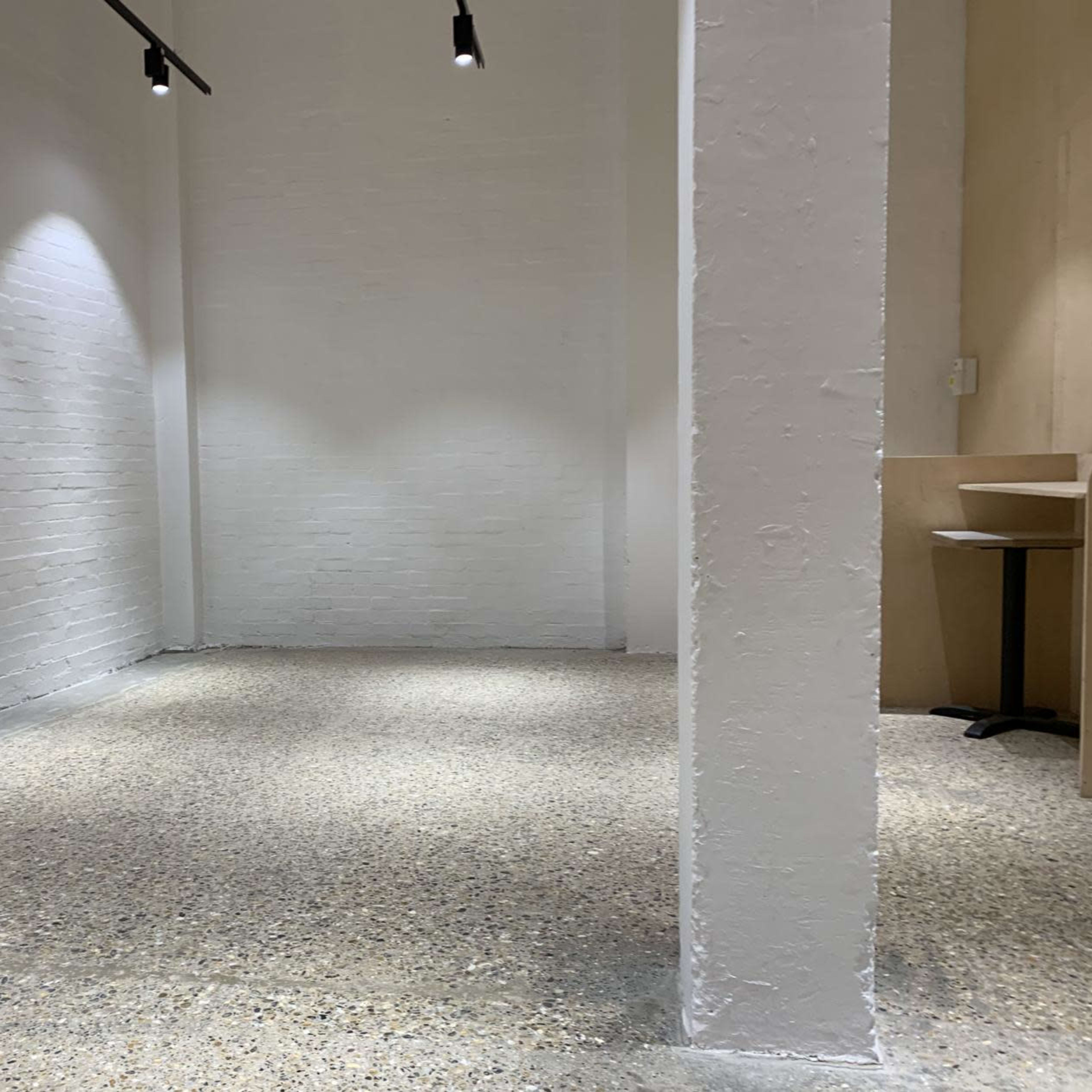 A minimalist, empty room with white walls, a concrete floor, and a single column.