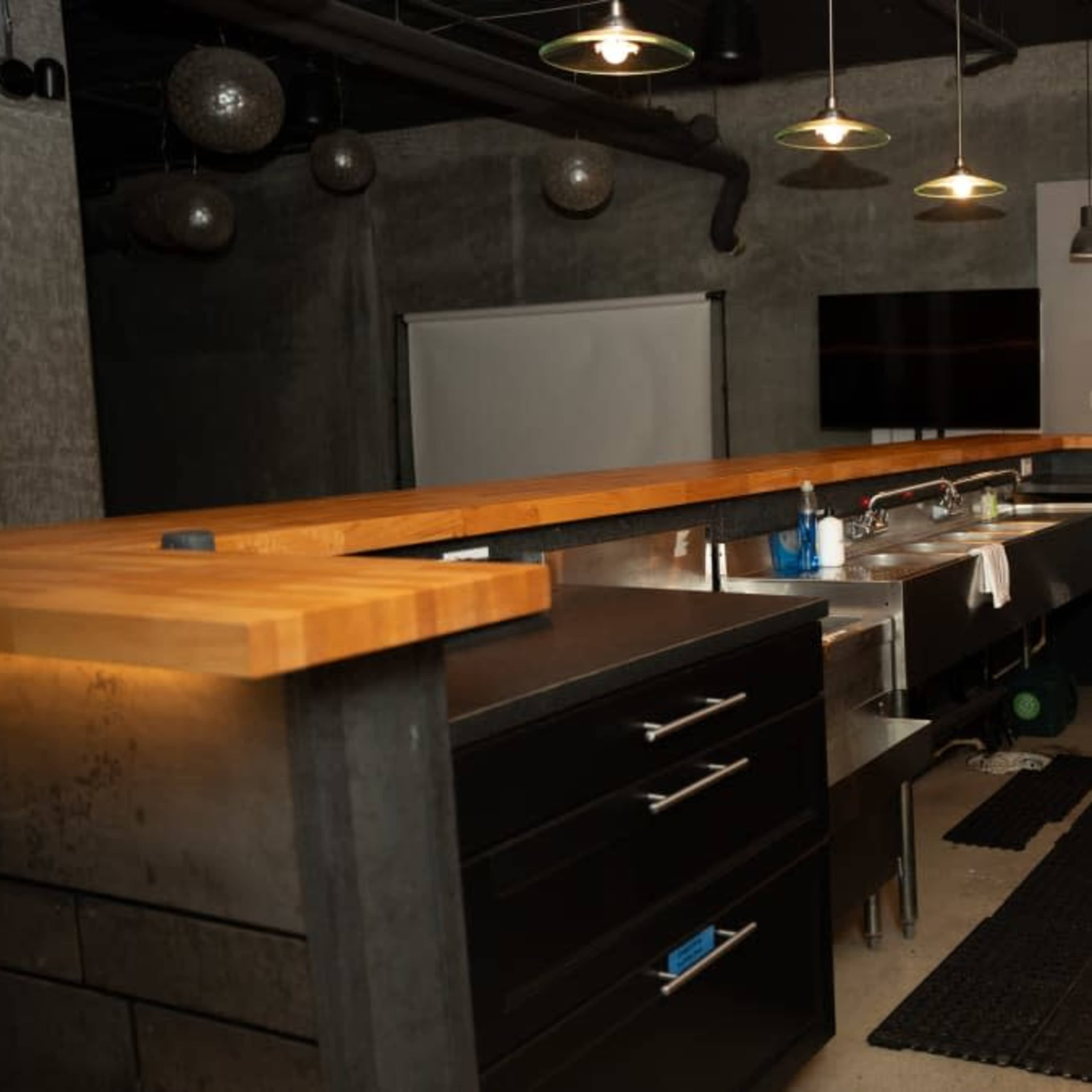A modern kitchen with stainless steel sinks and dark cabinetry, featuring a wooden countertop and a black mat on the floor.