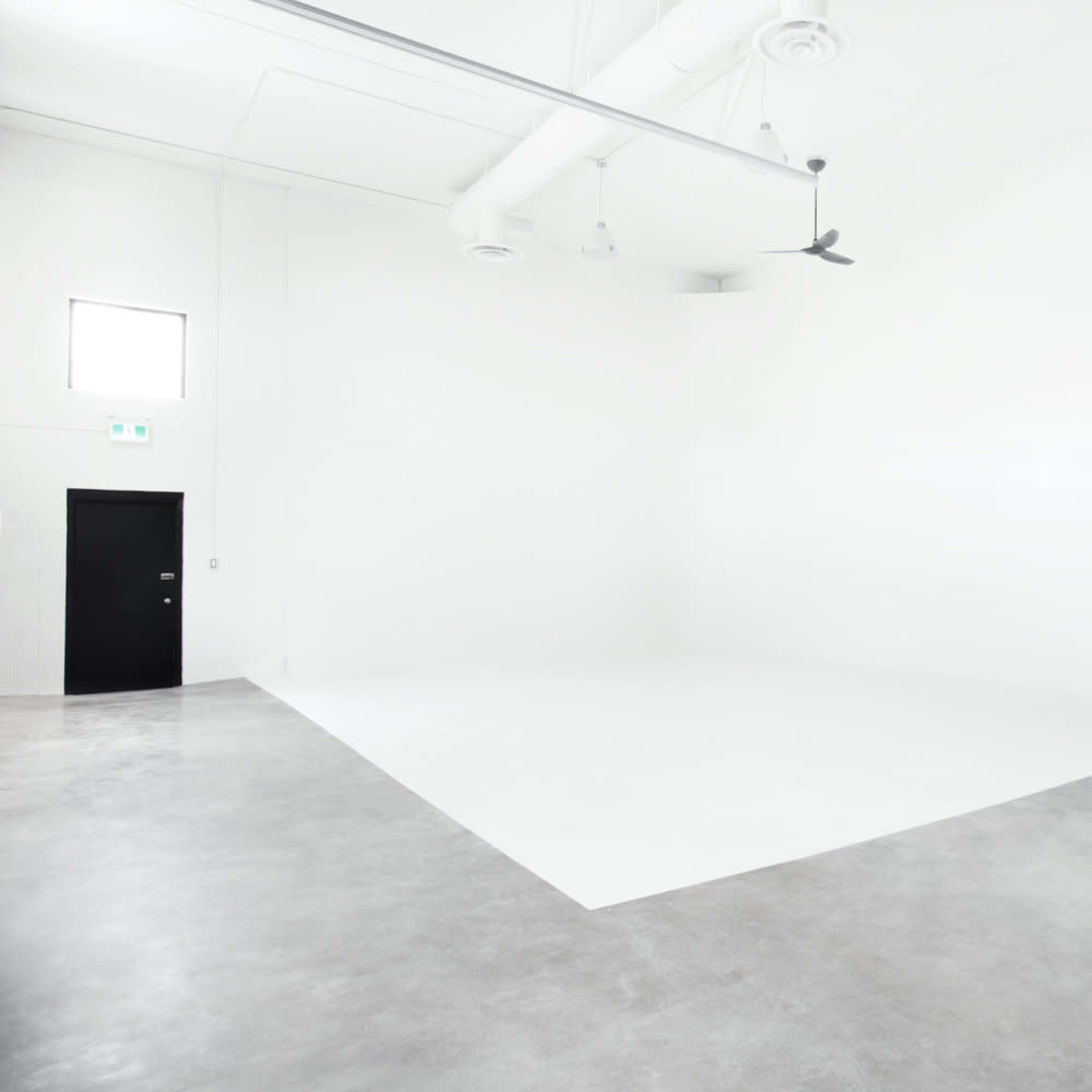 A spacious, minimalist room with white walls, a concrete floor, and a large, empty area.