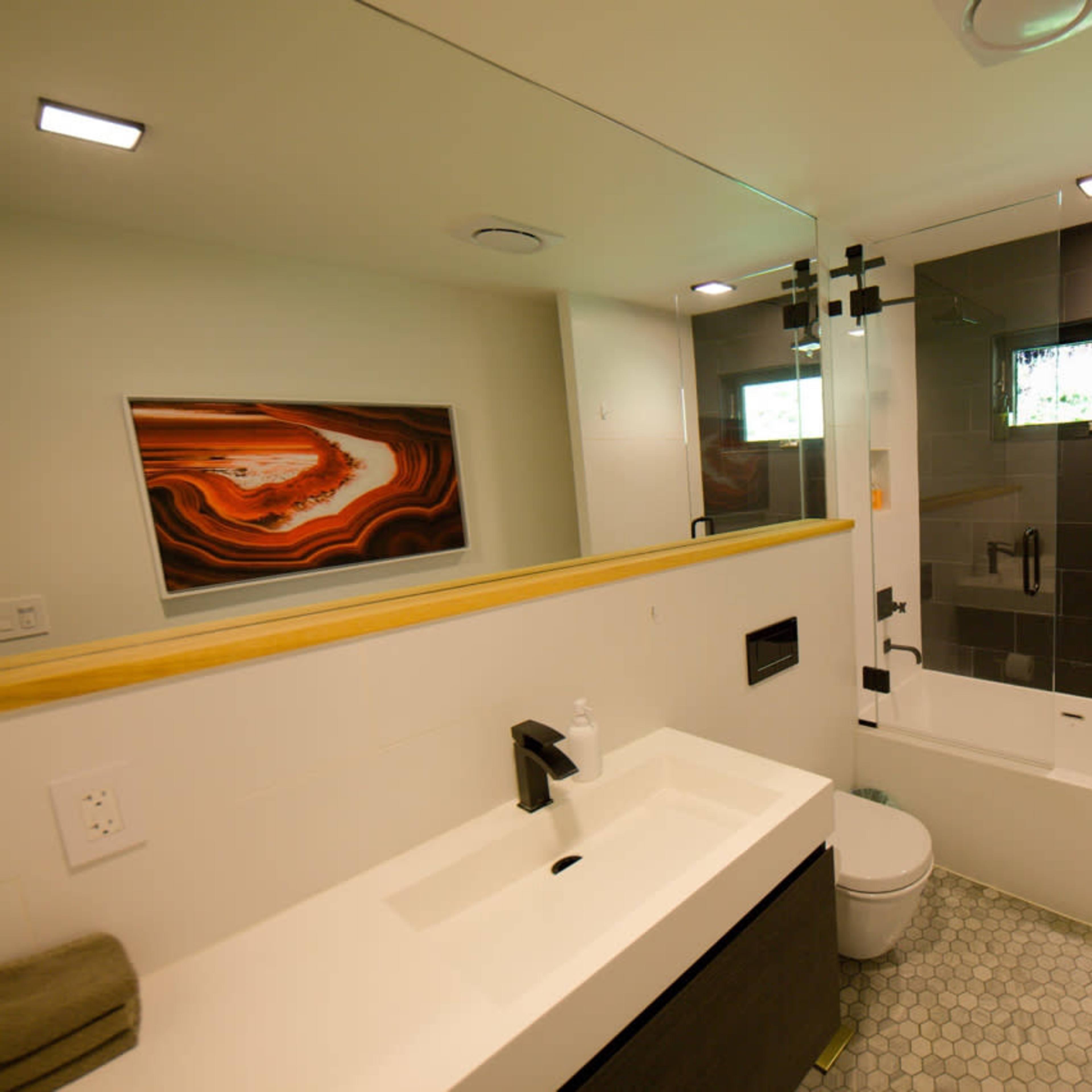 The bathroom features a modern design with a white sink, a bathtub with a glass shower enclosure, and a large mirror above the vanity.
