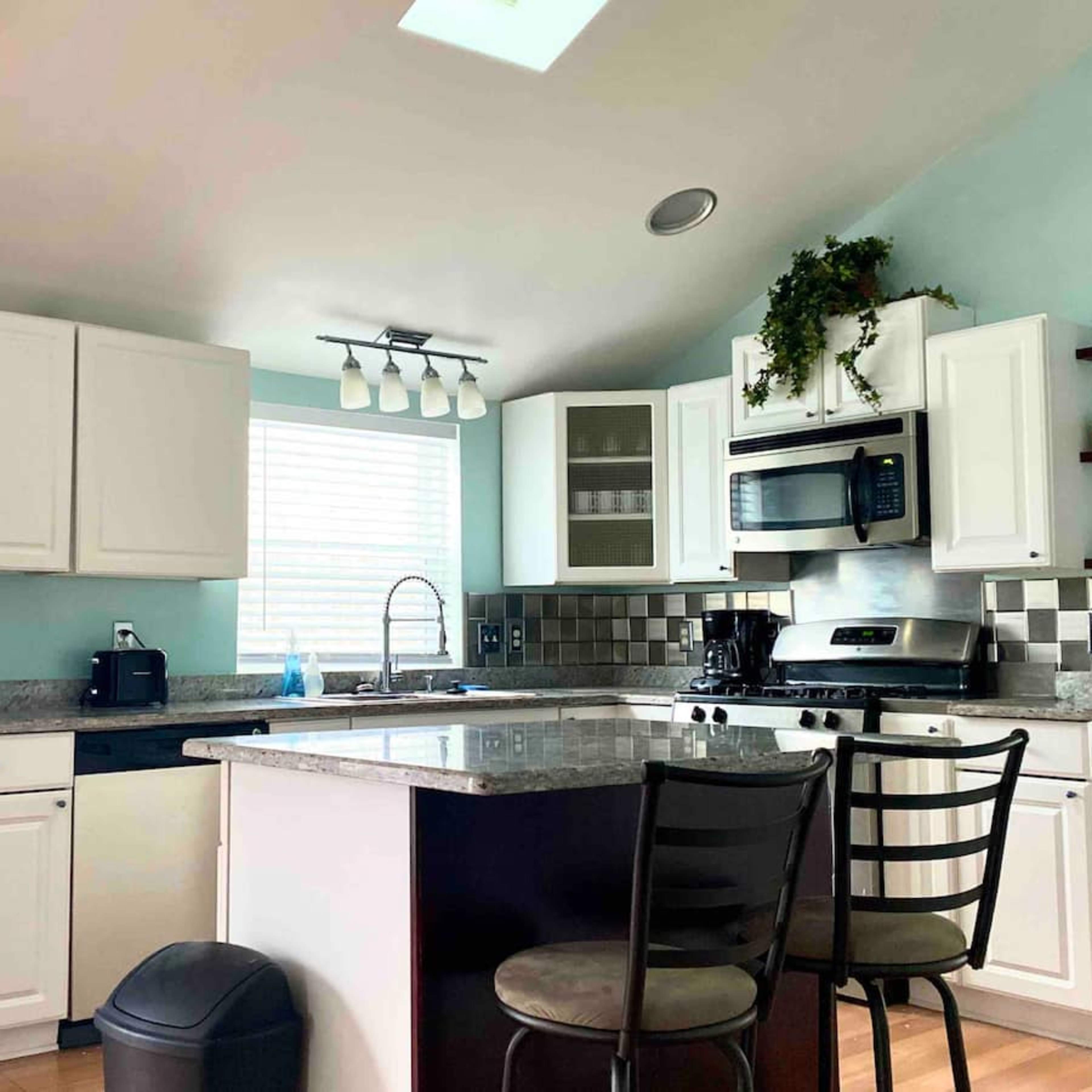 A modern kitchen with white cabinets, a granite countertop, a black refrigerator, and stainless steel appliances.