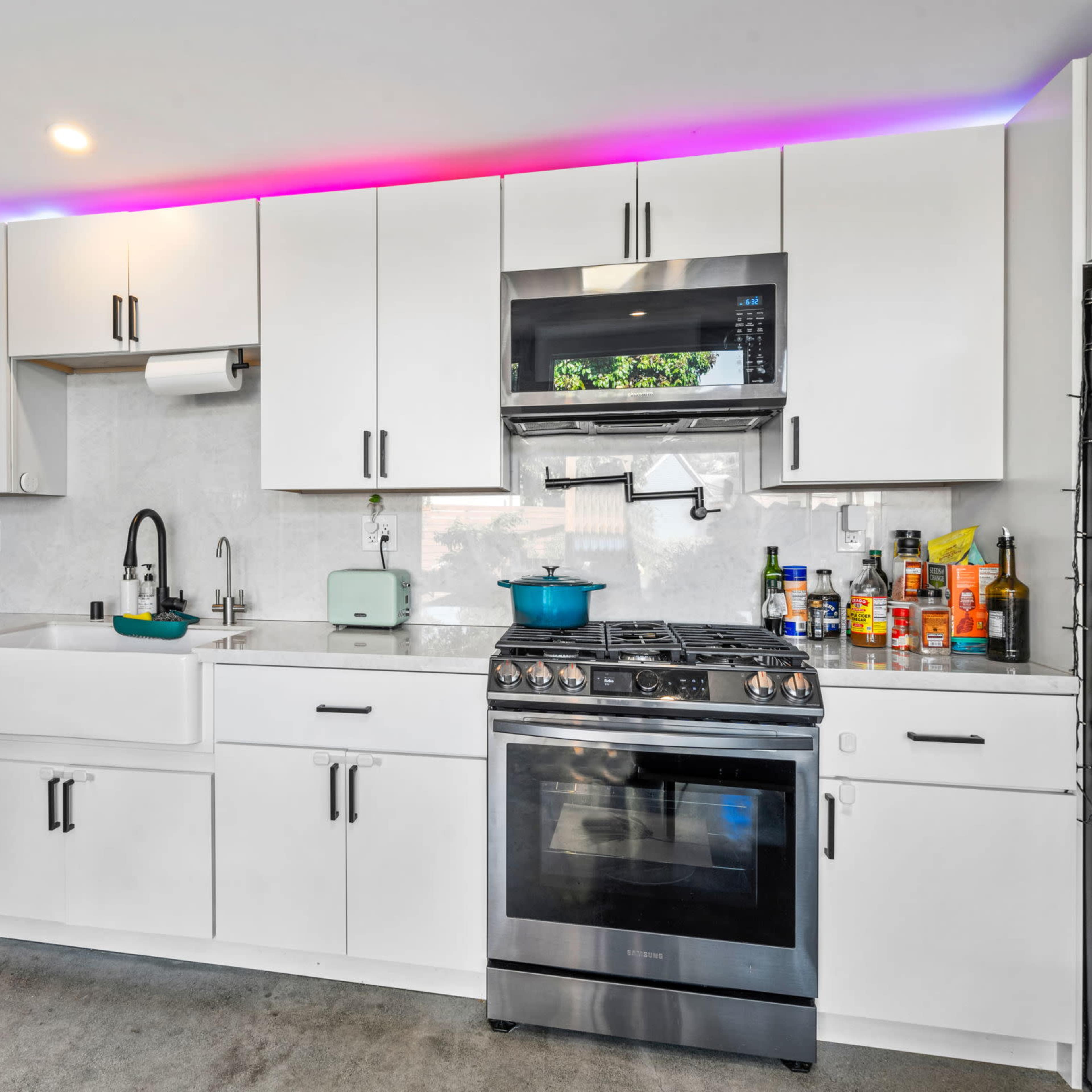 A modern kitchen features white cabinets, stainless steel appliances, and a colorful LED light strip along the upper edge.