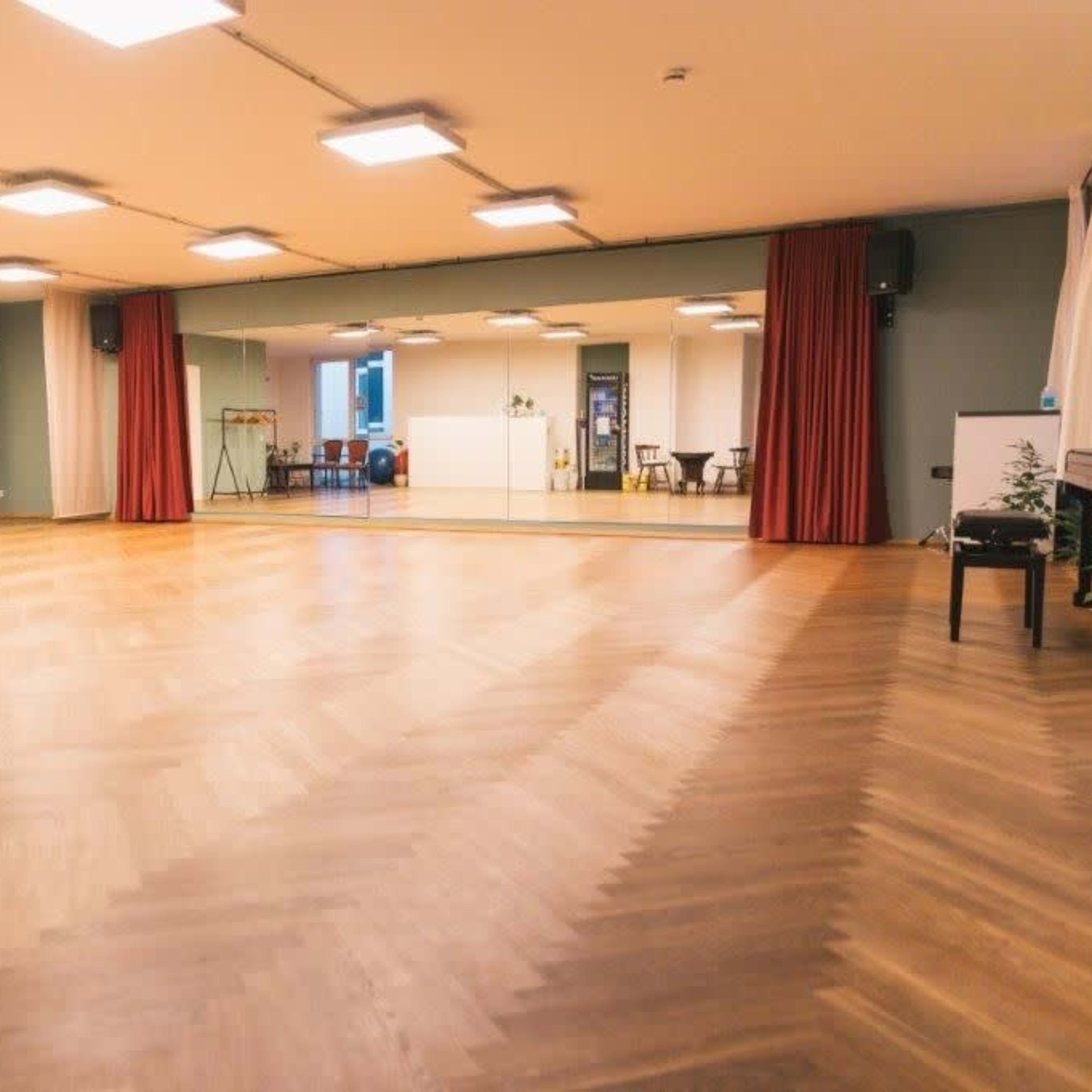 A spacious, empty room with wooden floors, a large mirror on one wall, and several doors along another wall.