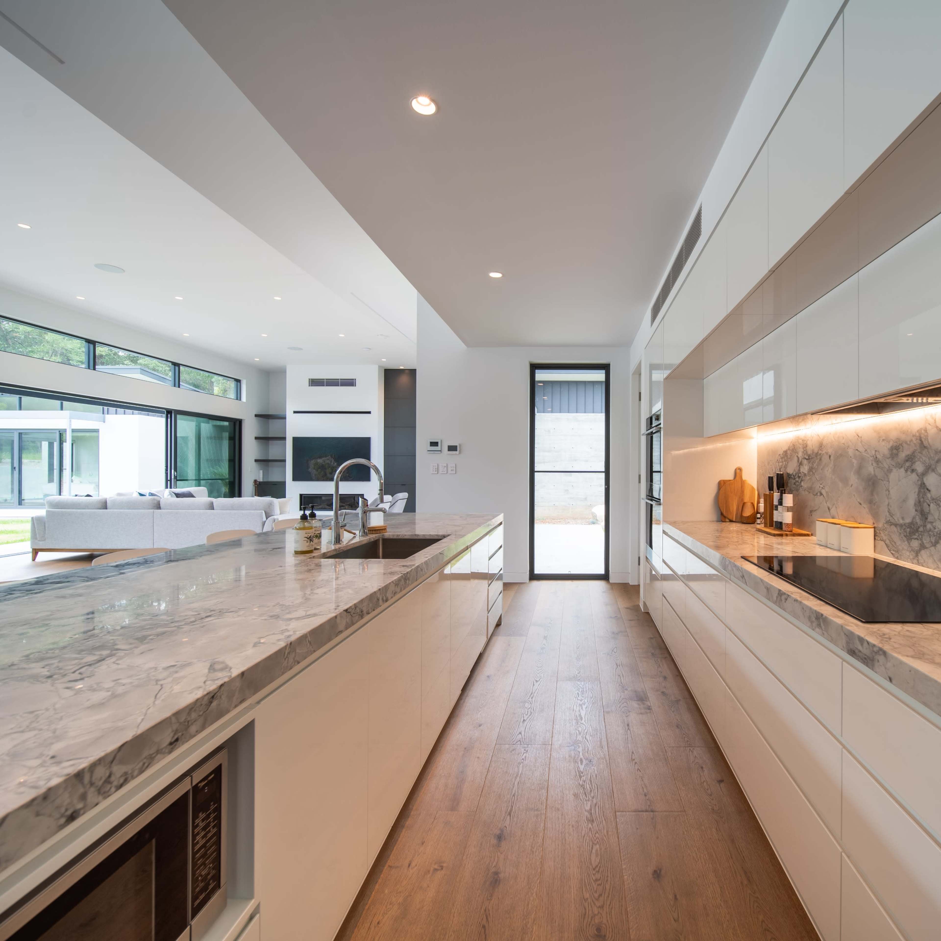 A modern kitchen with white cabinetry, a marble countertop, and large windows overlooking an outdoor space.