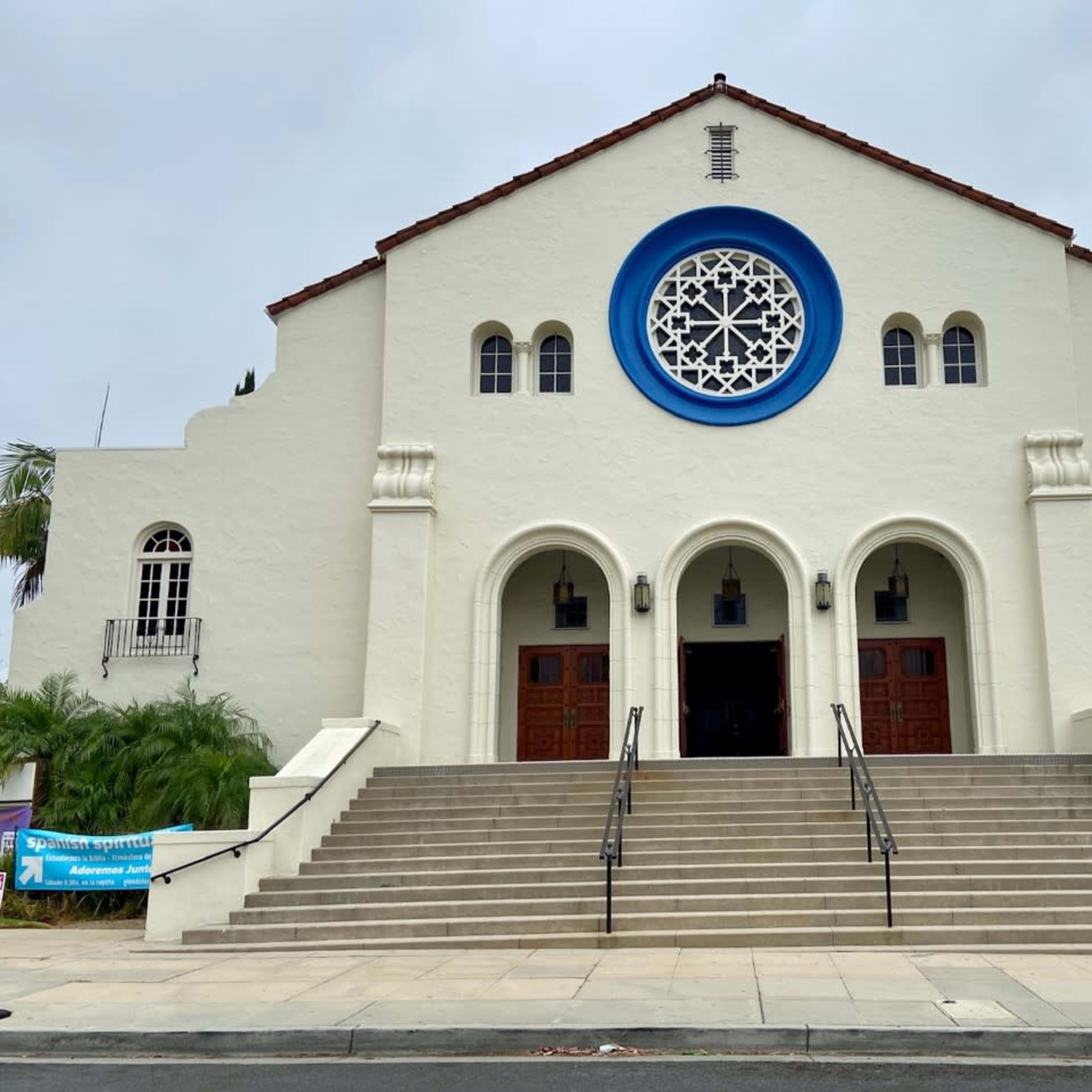 A large, white building with a distinctive circular window and two wooden doors, flanked by a flight of steps leading up to the entrance.