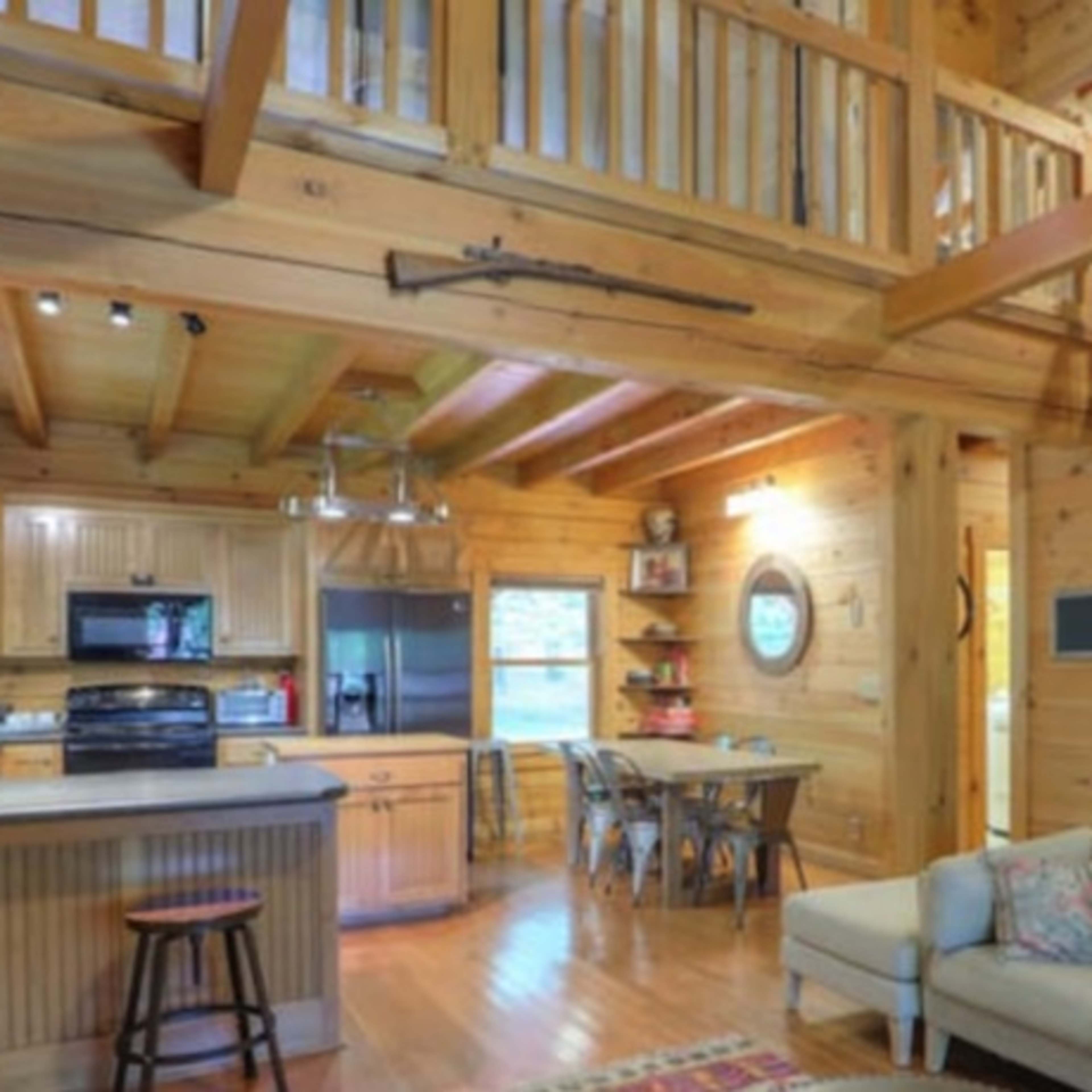 A wooden cabin interior featuring an open layout with a kitchen, dining area, and a living space, along with a staircase leading to a loft.