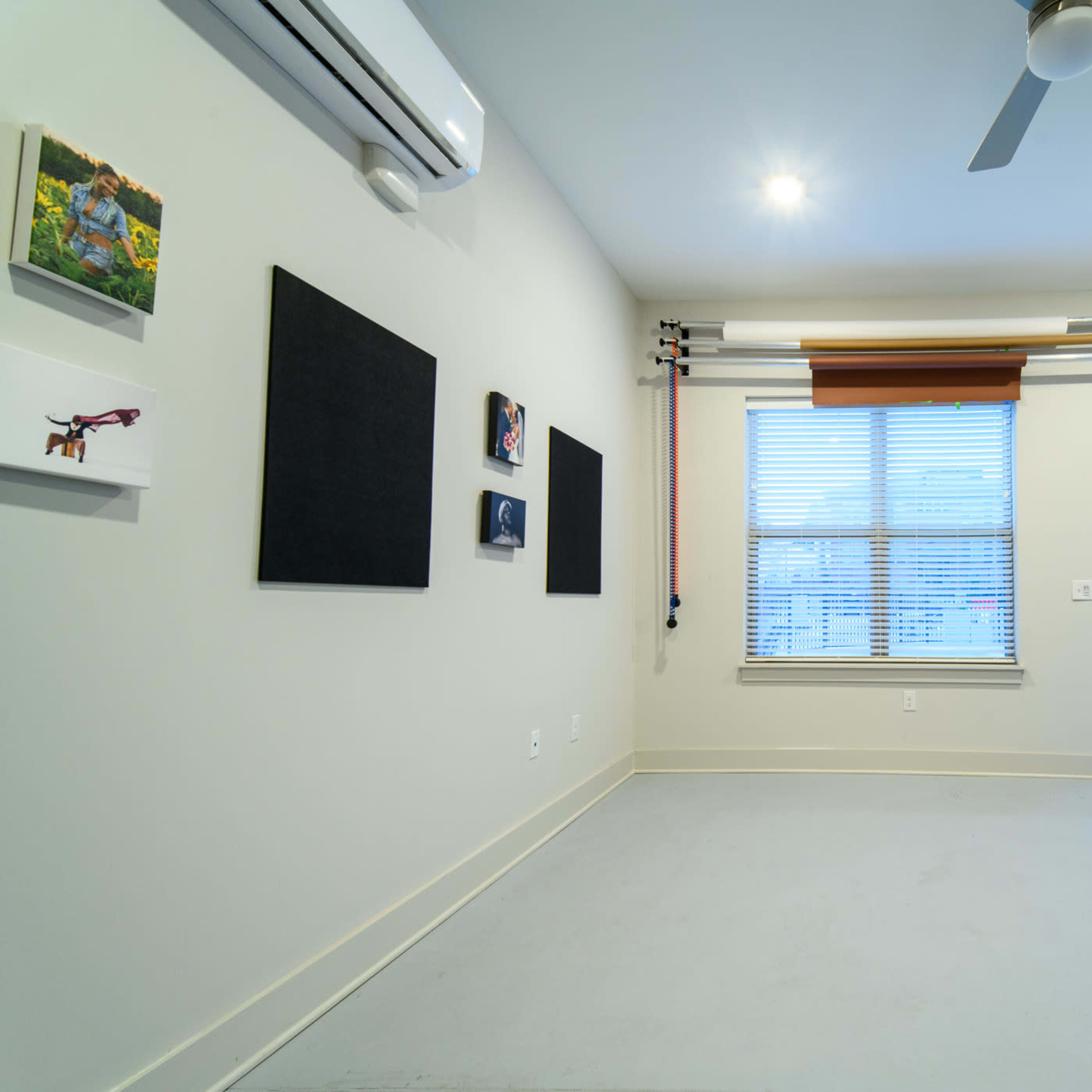 A sparsely furnished room with two black wall panels, a window with blinds, and a chair near the door.
