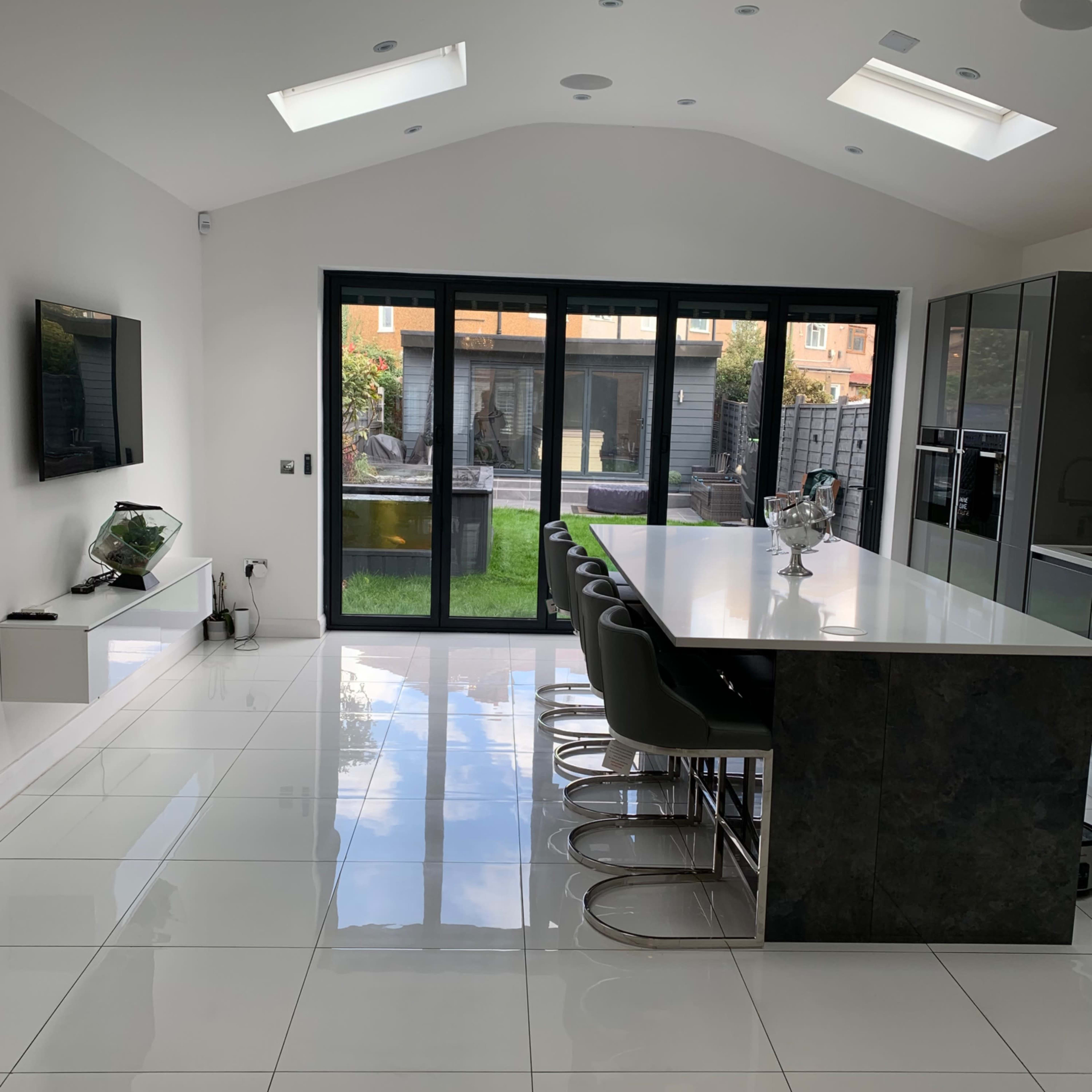 A modern kitchen with a large island bar, sleek cabinetry, and floor-to-ceiling glass doors leading to an outdoor garden.