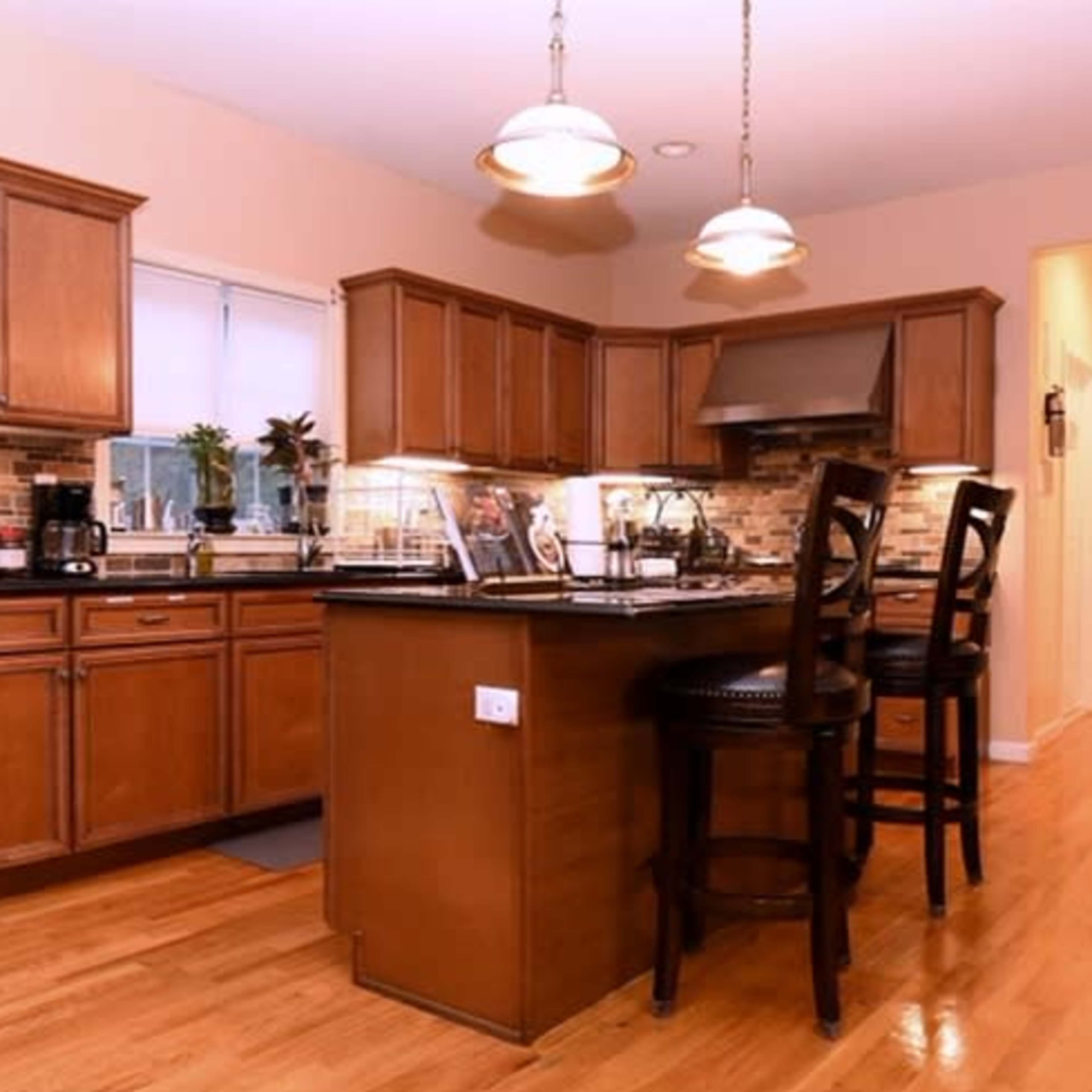 A kitchen with wooden cabinets, stainless steel appliances, and a central island with three bar stools.