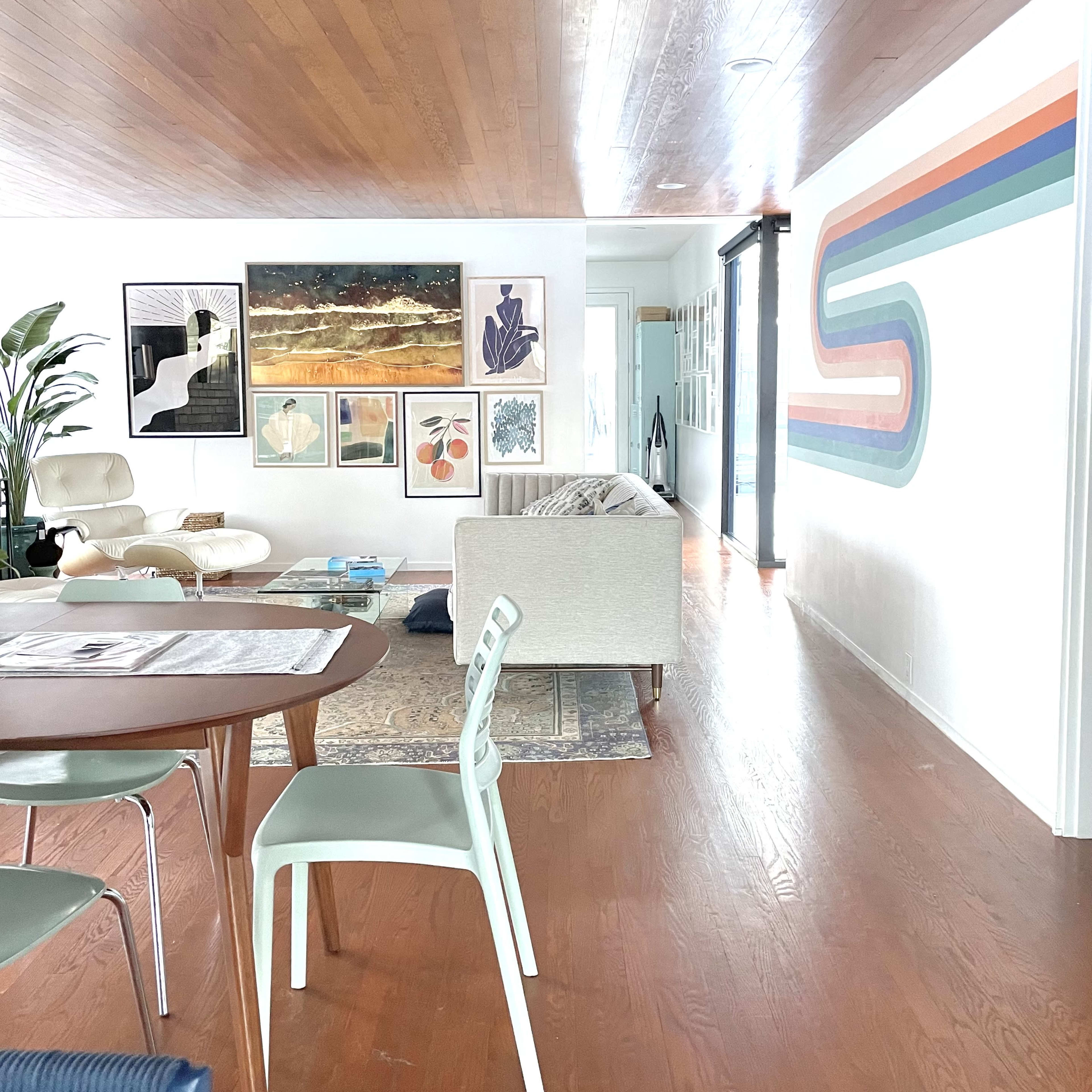 A spacious interior features a dining area with a wooden table, chairs, and a wall adorned with colorful artwork.