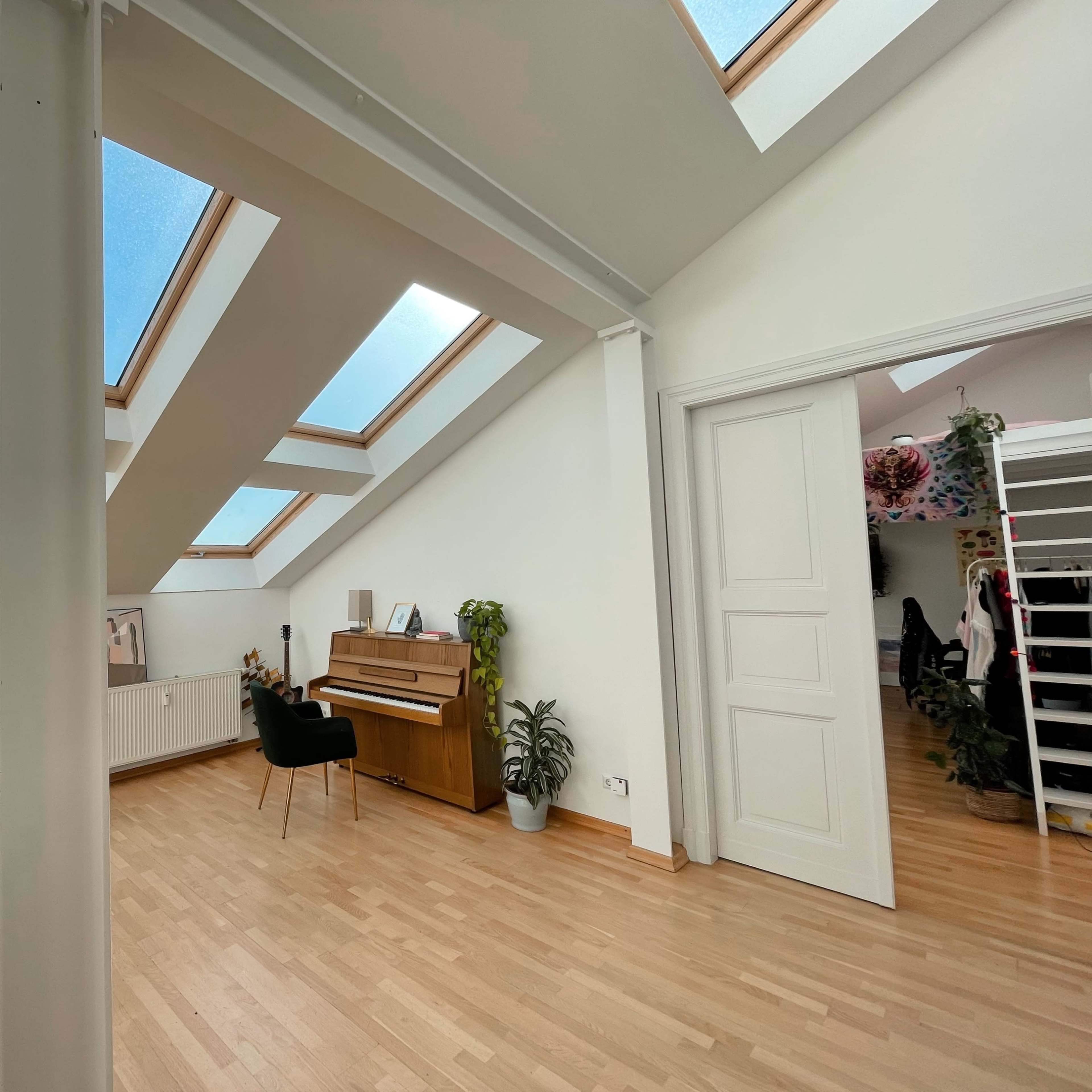 A bright room with a piano, plants, and skylights illuminating the space.