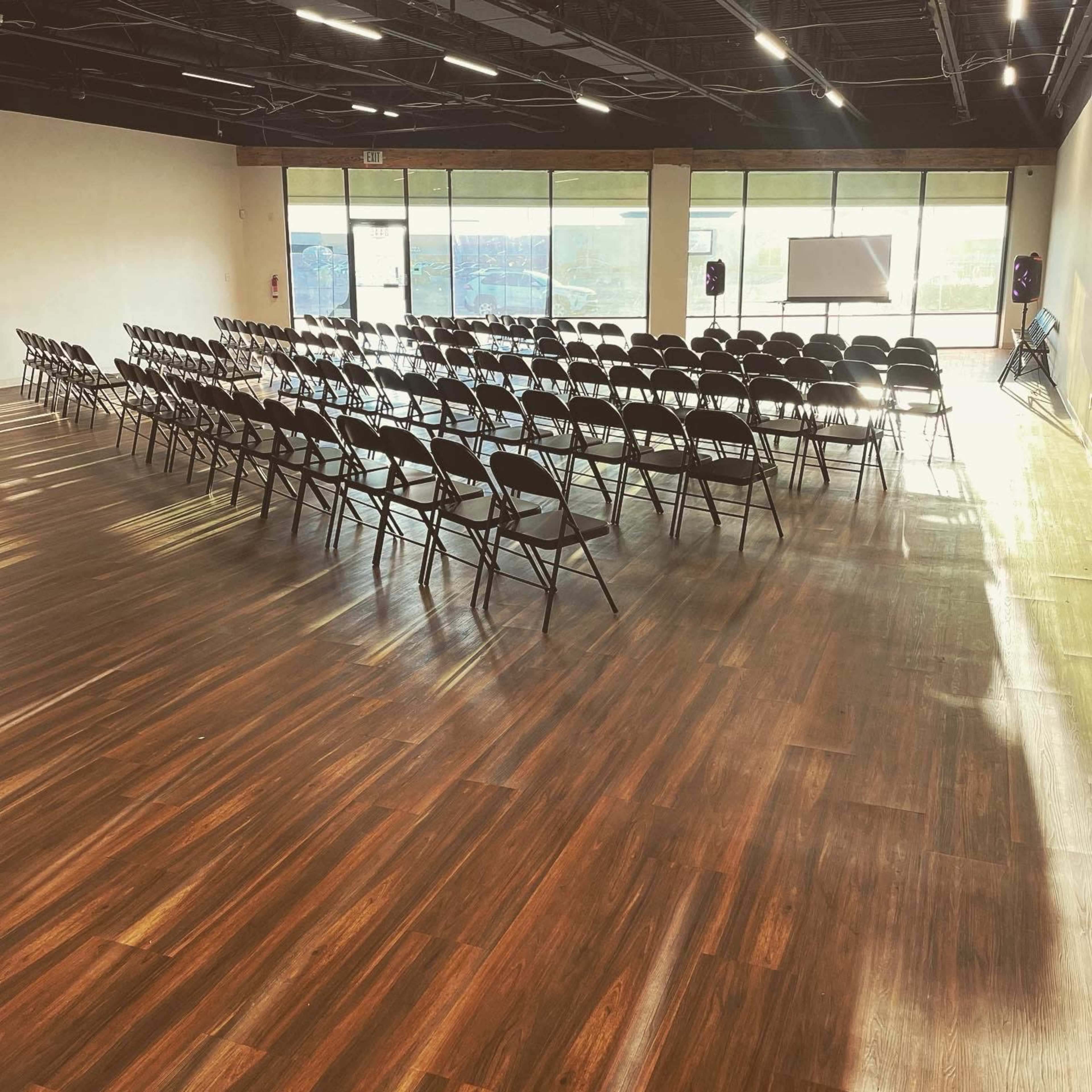 A spacious room with rows of empty chairs set up for an event, featuring large windows that allow natural light to fill the space.