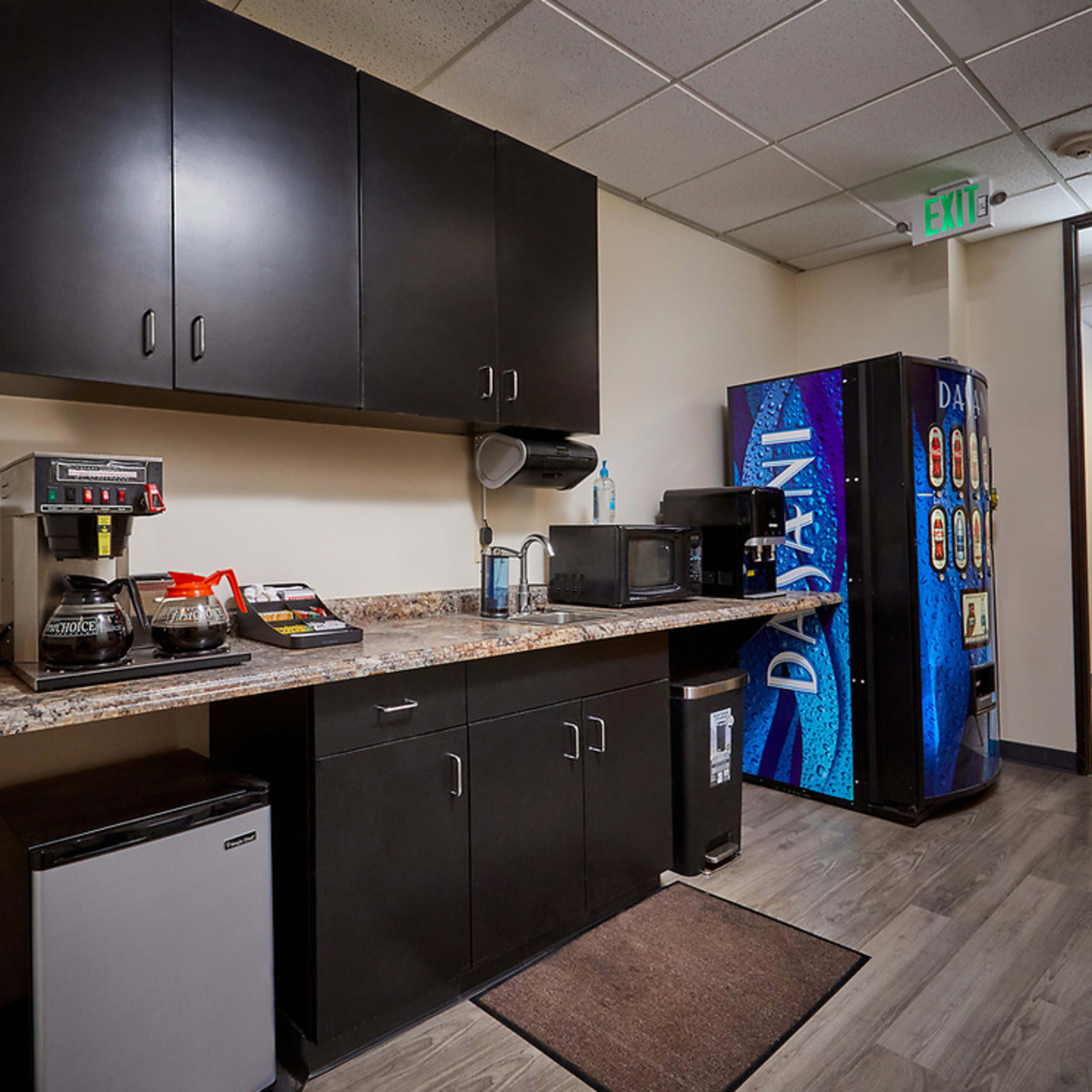 A break room with dark cabinetry, a coffee maker, a microwave, a vending machine, and a mini refrigerator along a countertop.