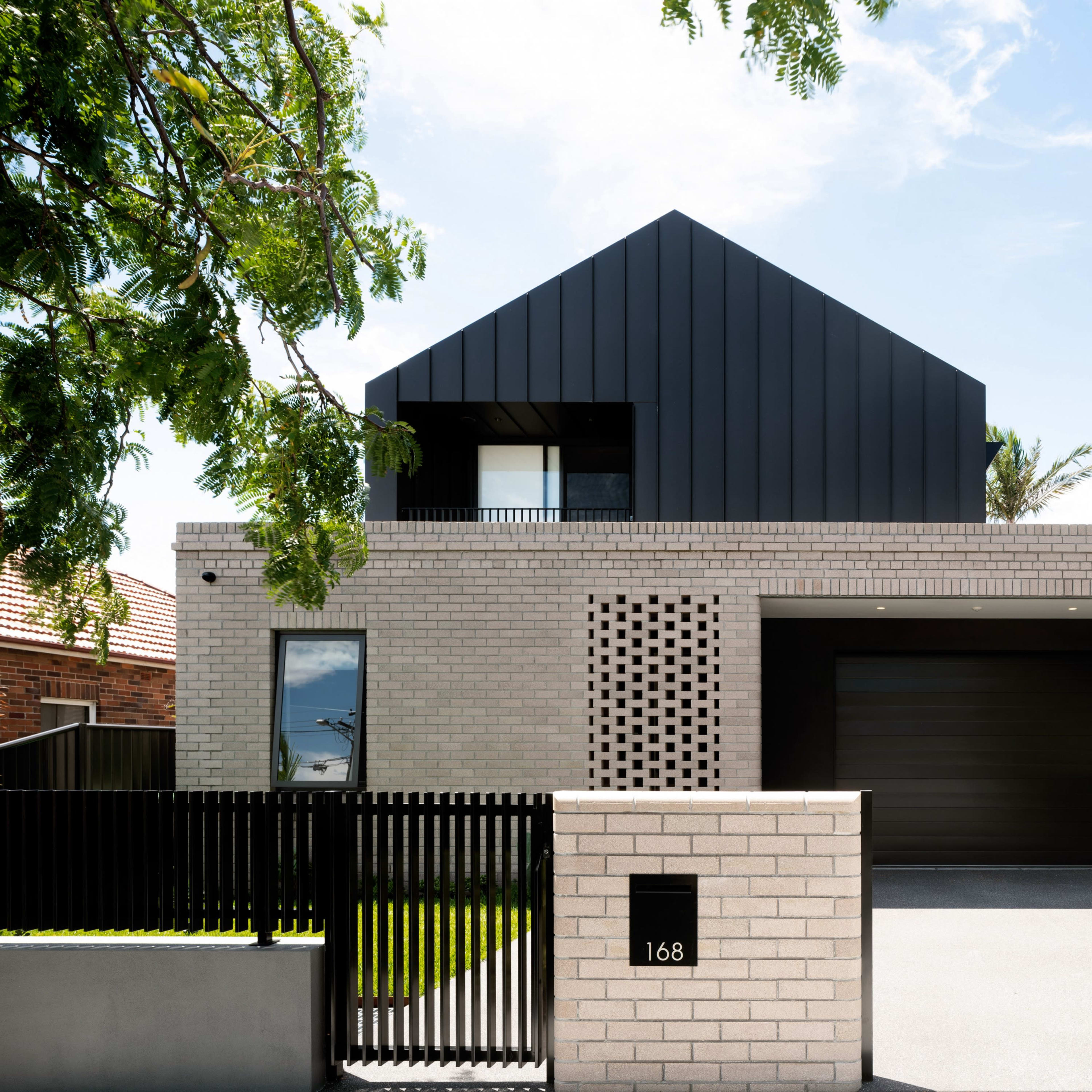 A modern two-story house with a combination of brick and black metal siding, featuring a driveway and a decorative fence.