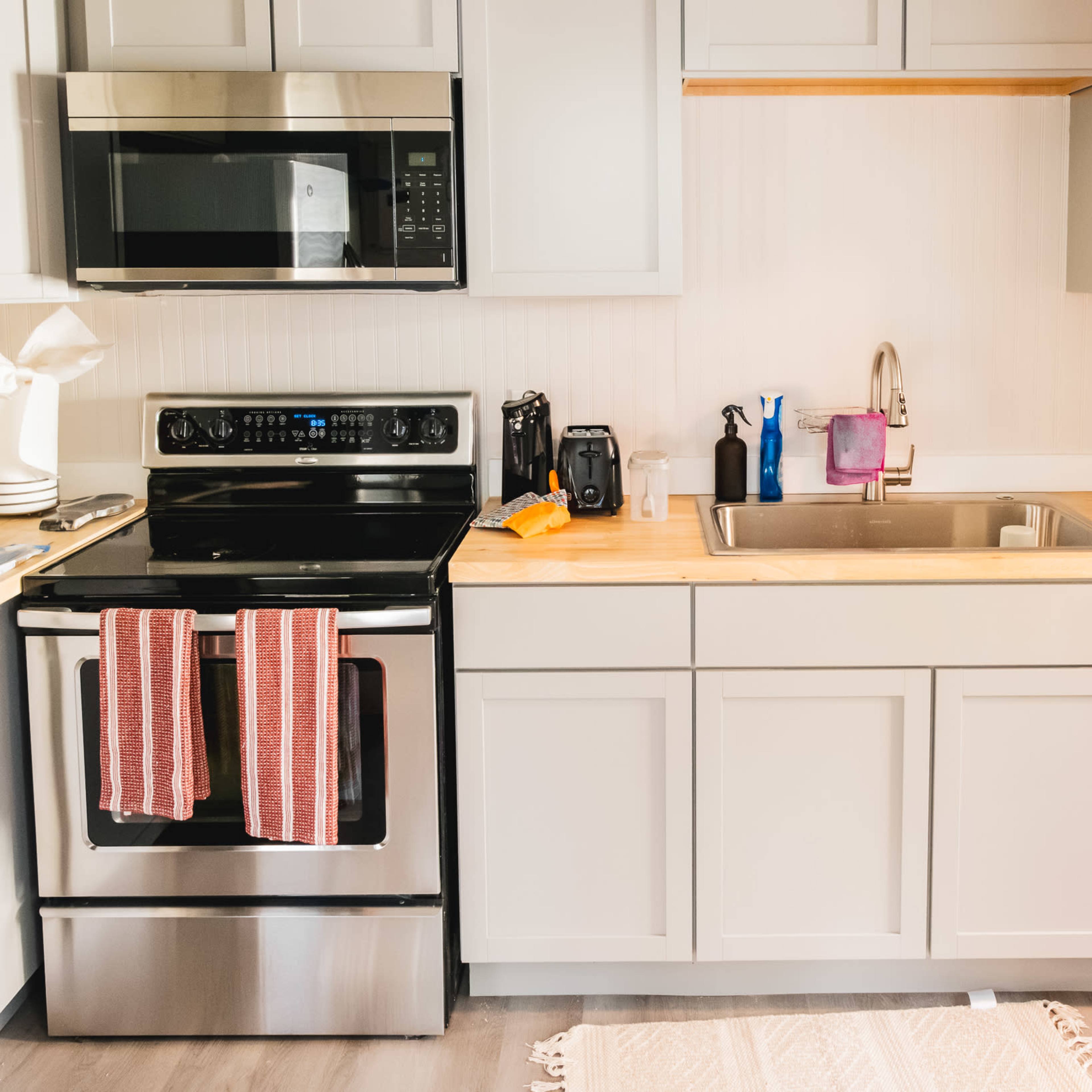 A modern kitchen features stainless steel appliances, a wooden countertop, and a sink, with red-striped towels hanging from the stove.