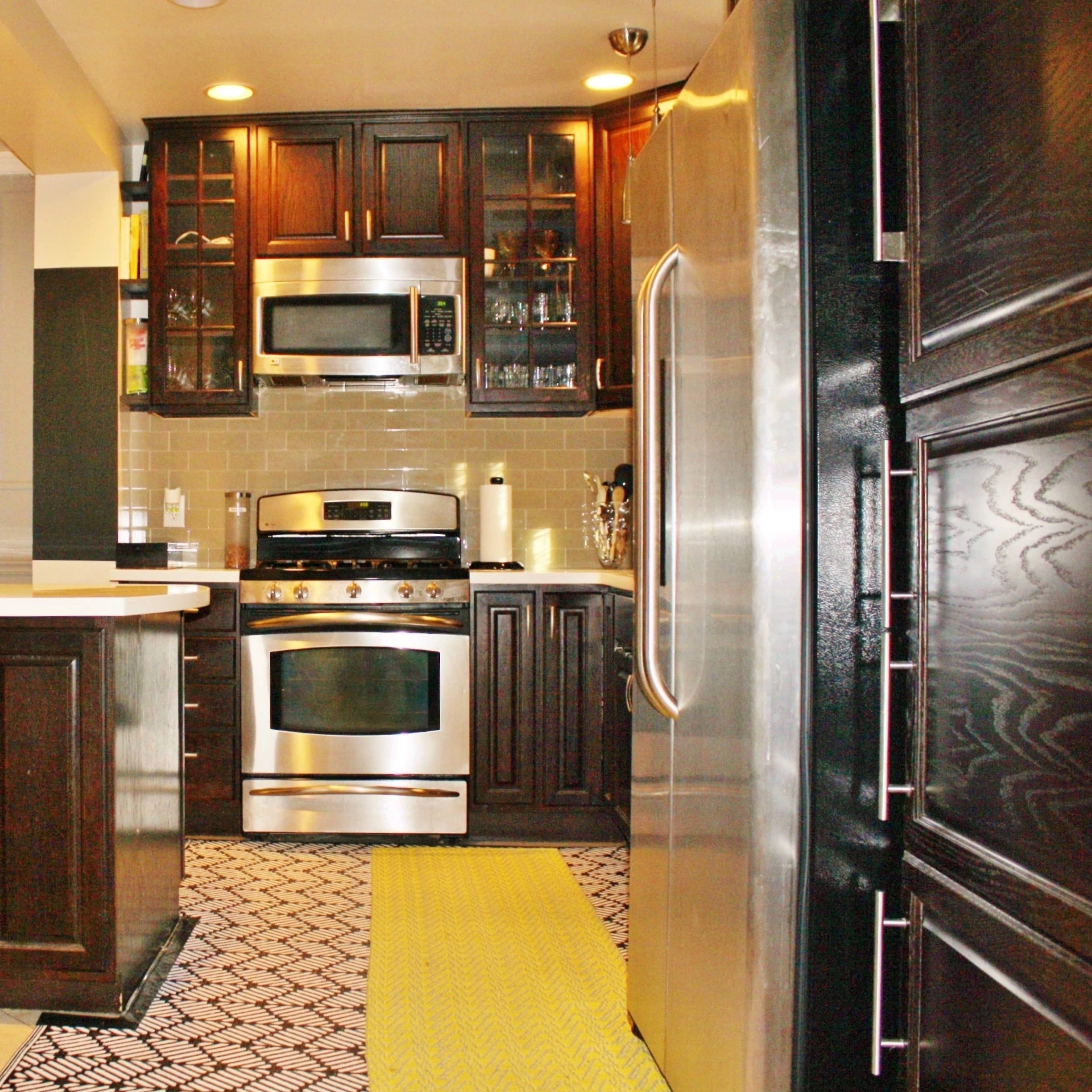 A modern kitchen featuring dark wooden cabinets, stainless steel appliances, and a patterned floor.