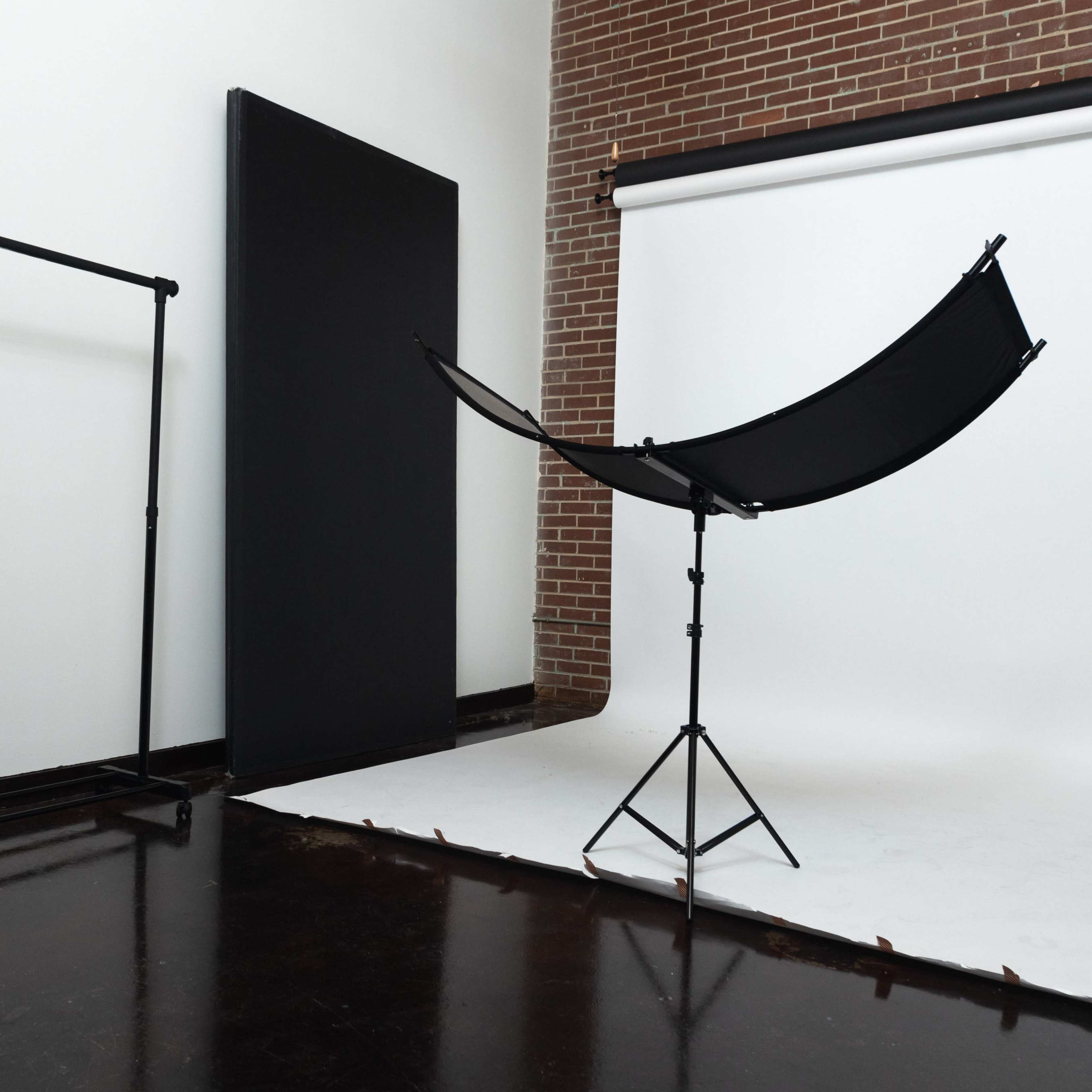 A photography studio with a backdrop, a large black reflector on a stand, and an equipment rack.