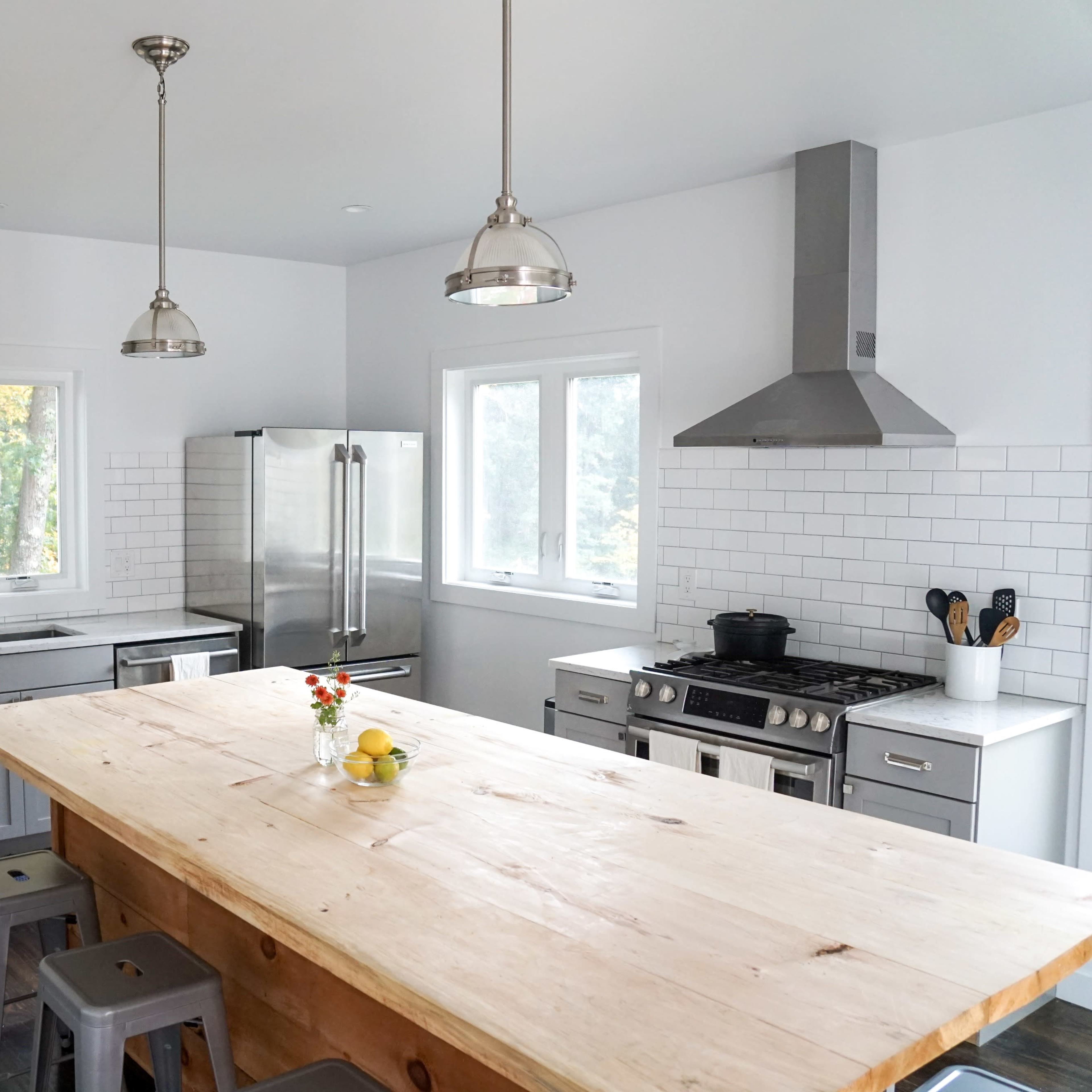 A modern kitchen features a large wooden island, stainless steel appliances, gray cabinets, and white tile backsplash.
