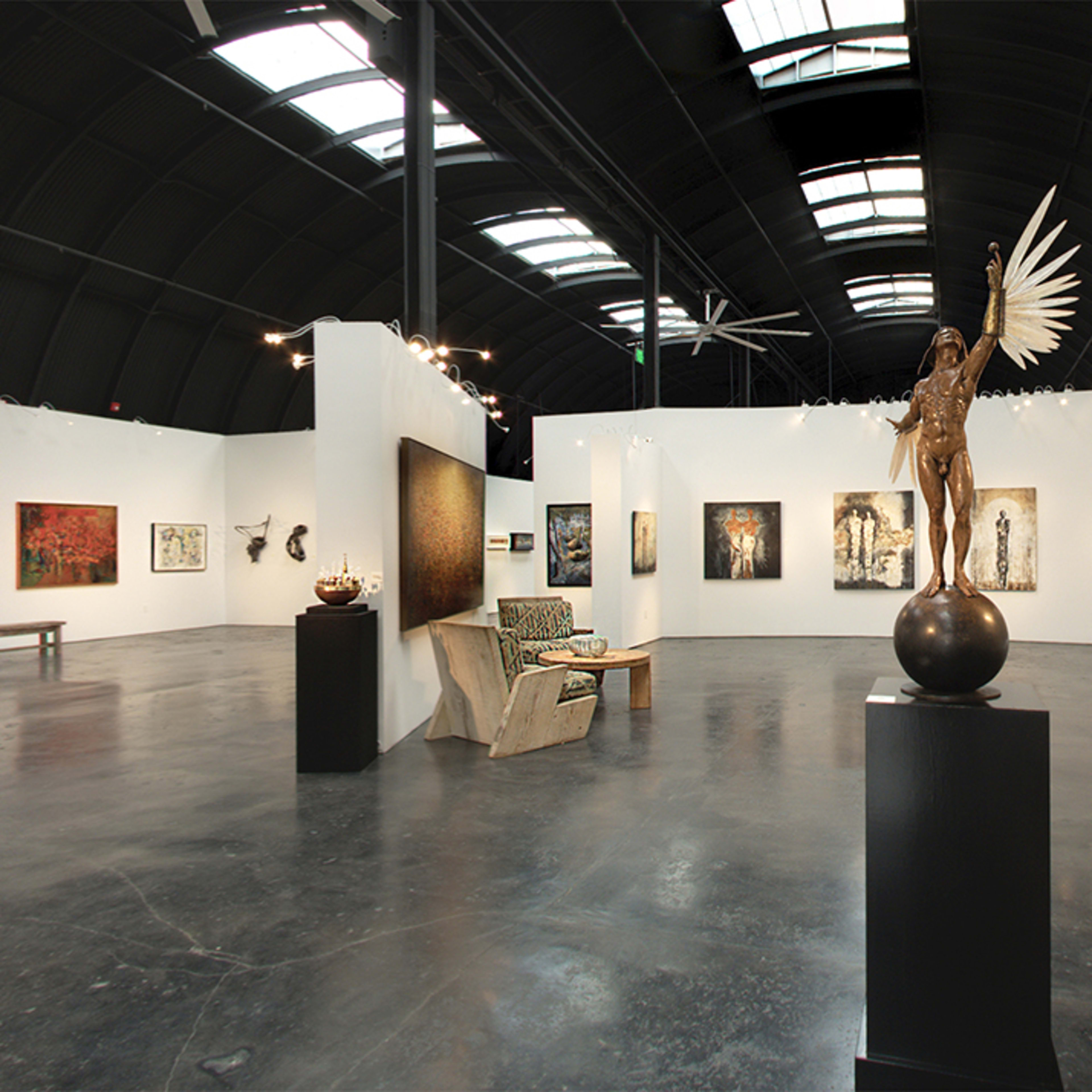 A spacious art gallery featuring various paintings and sculptures displayed on white walls and pedestals, with a polished concrete floor.