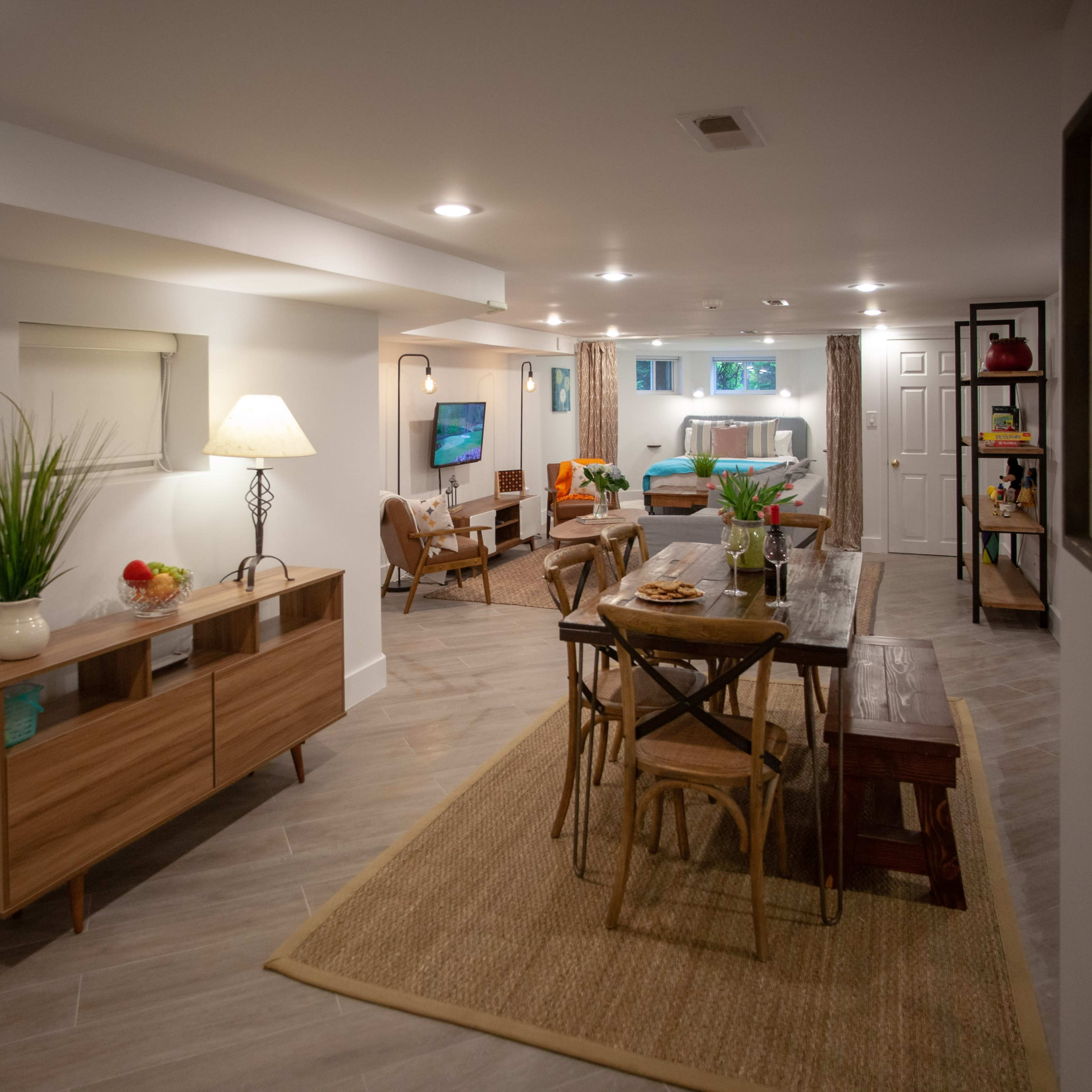 A modern, well-lit basement living space featuring a dining area, a cozy seating area, and decorative plants.
