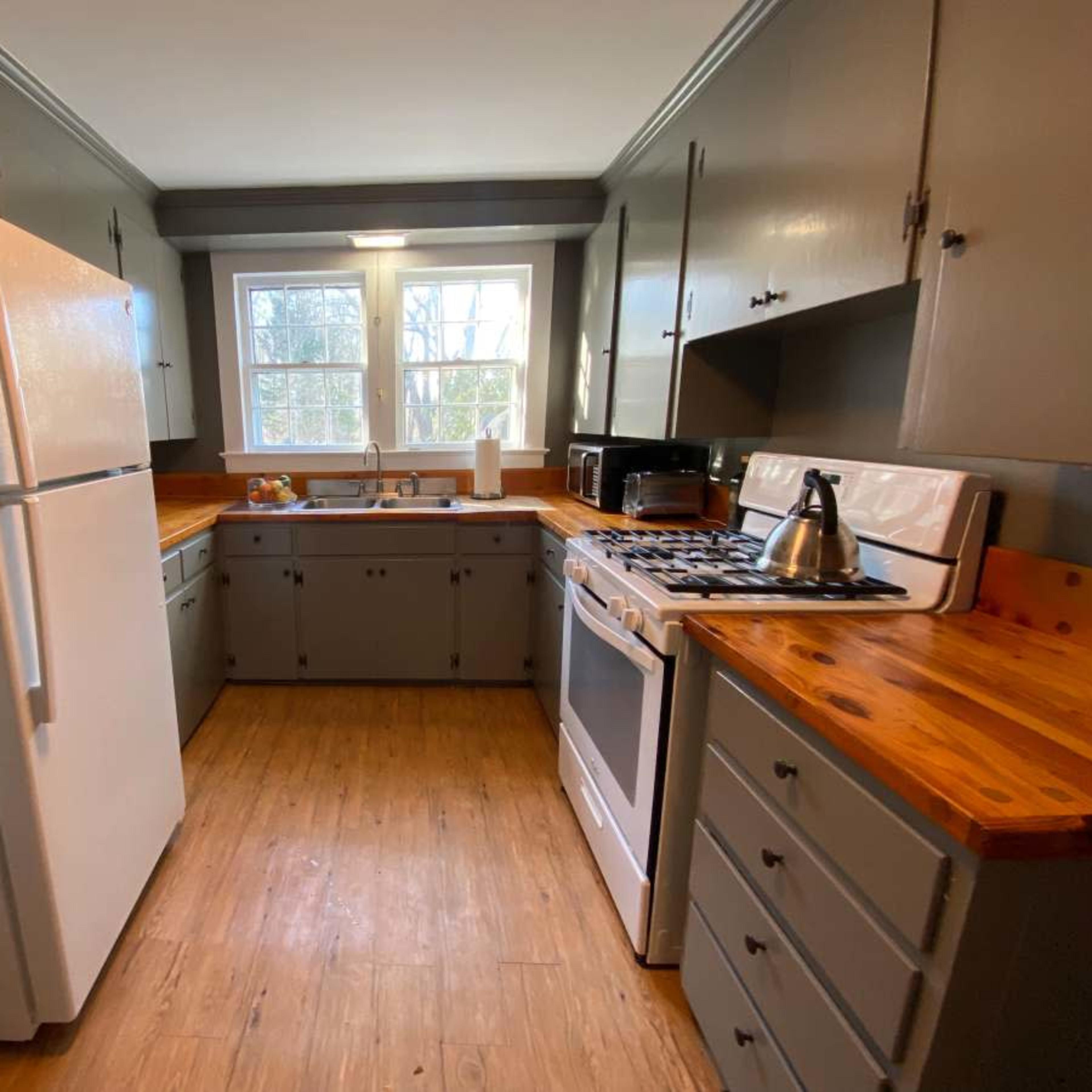 A kitchen features white appliances, wooden countertops, and gray cabinetry with a window providing natural light.