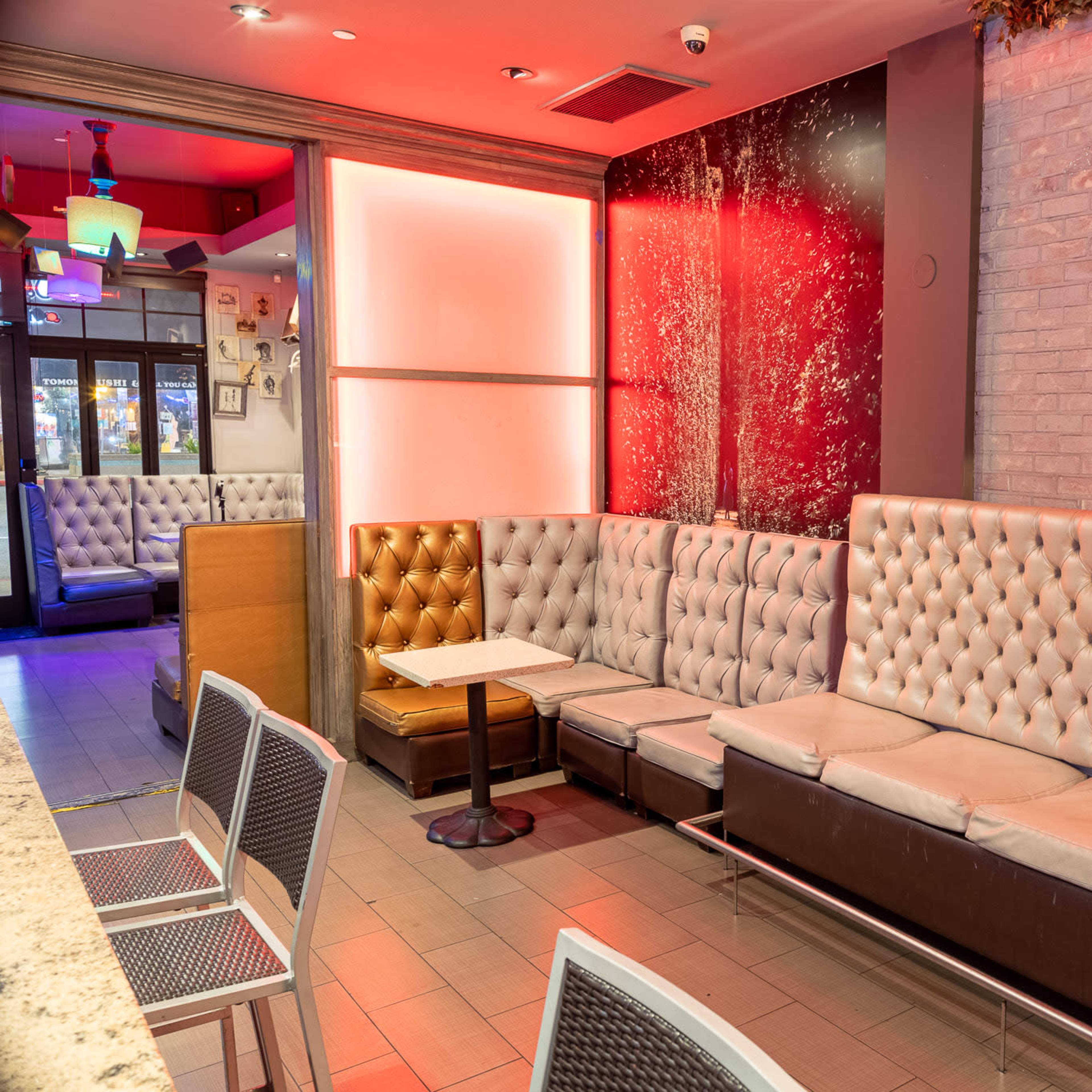 A modern seating area with tufted white benches, a small table, and a framed artwork on a brick wall, illuminated by red lighting.
