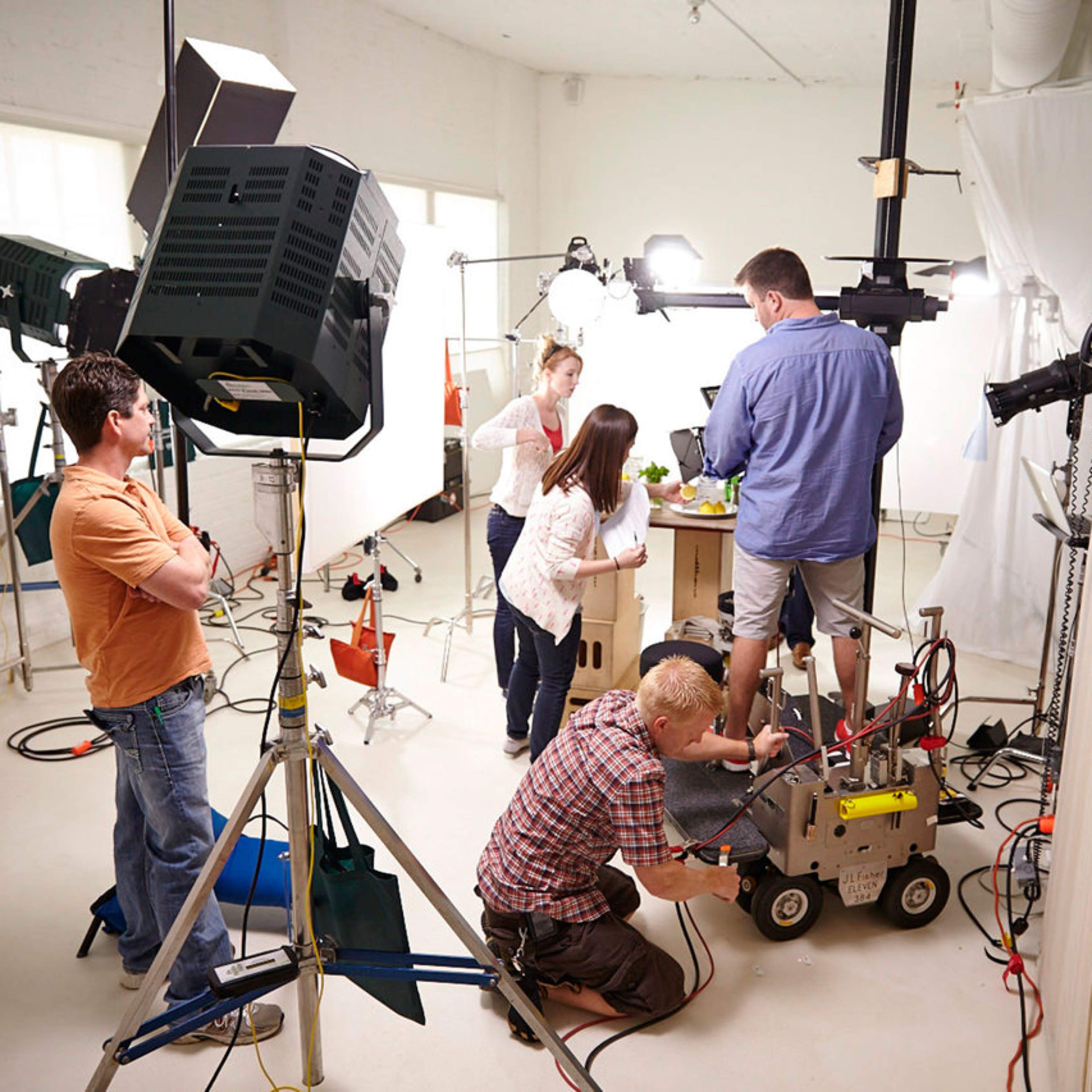 A group of five people work together in a studio setting, setting up equipment and adjusting a camera for a photoshoot.