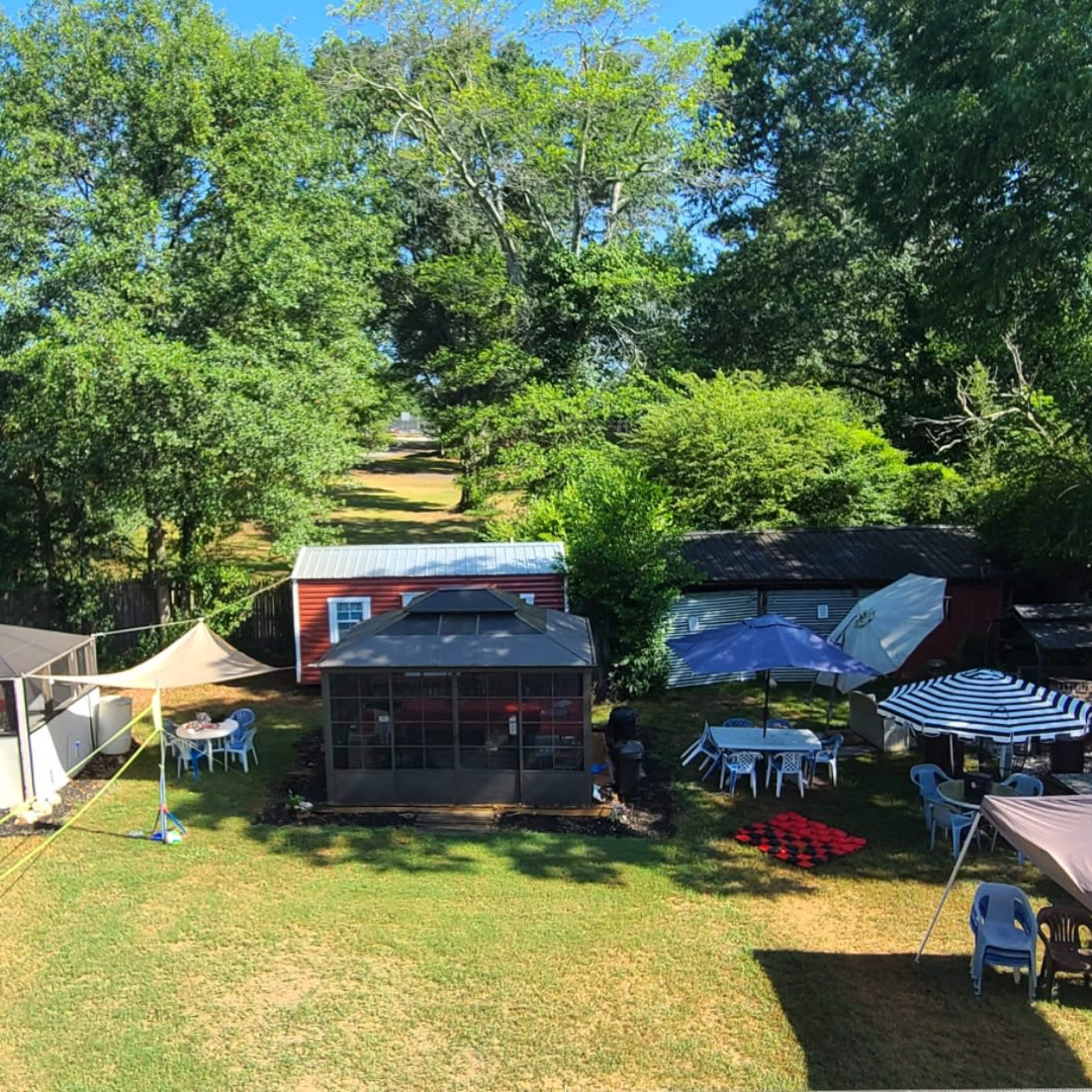 A backyard with several tents and tables set up among green grass and trees.
