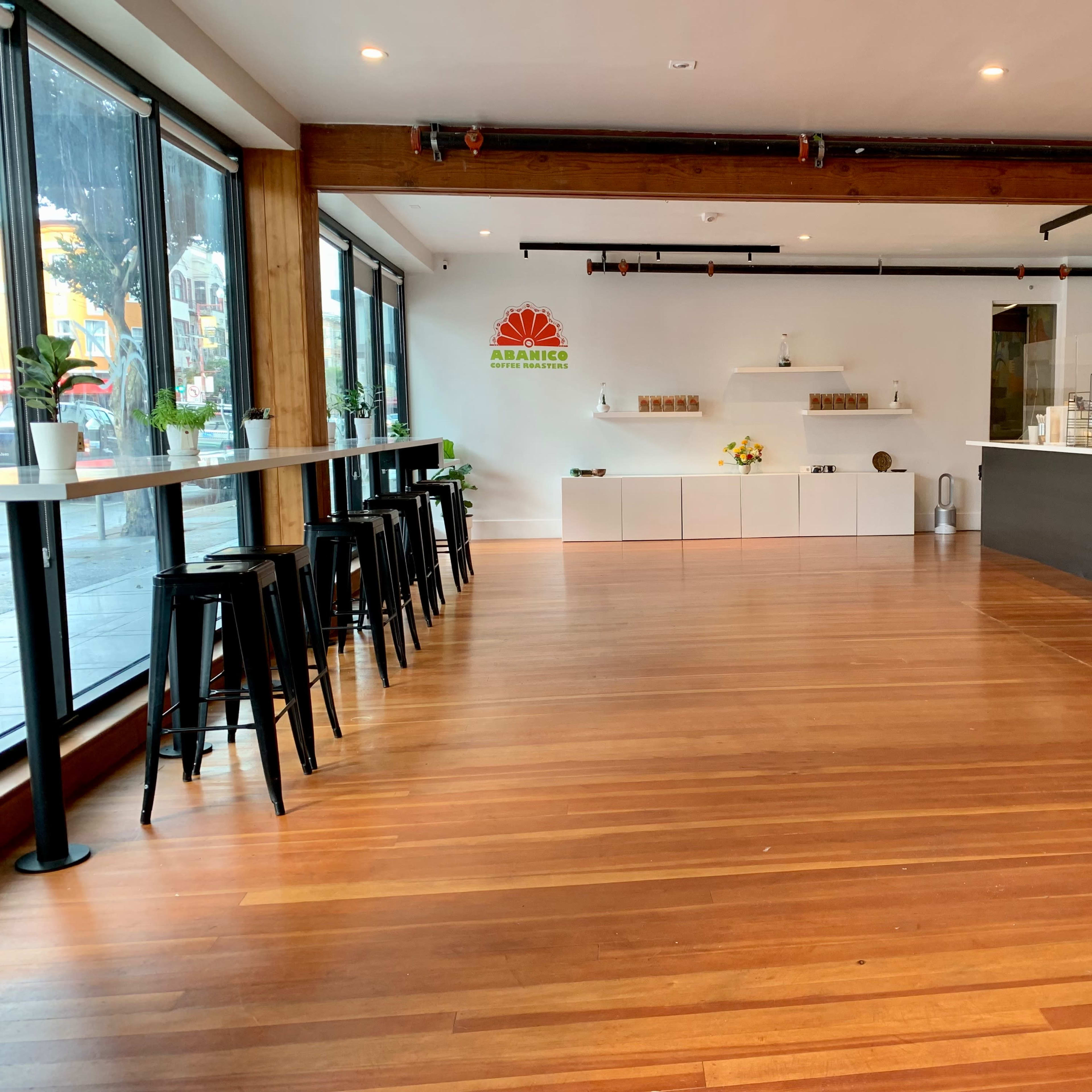 A spacious café interior with wooden floors, tall windows, and a counter on the right side.
