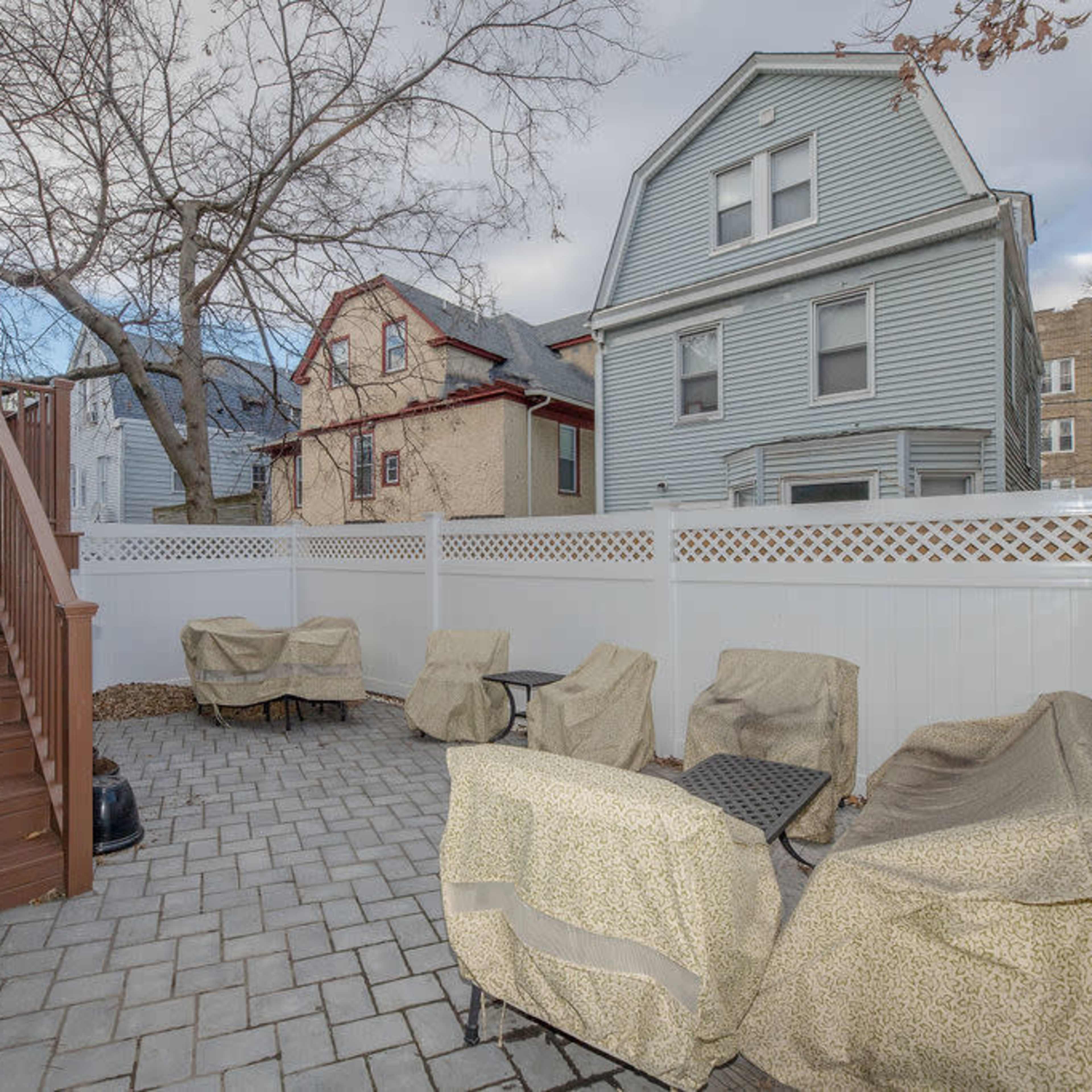 A backyard patio features a paved area with several covered seating arrangements and a staircase leading up to the house.
