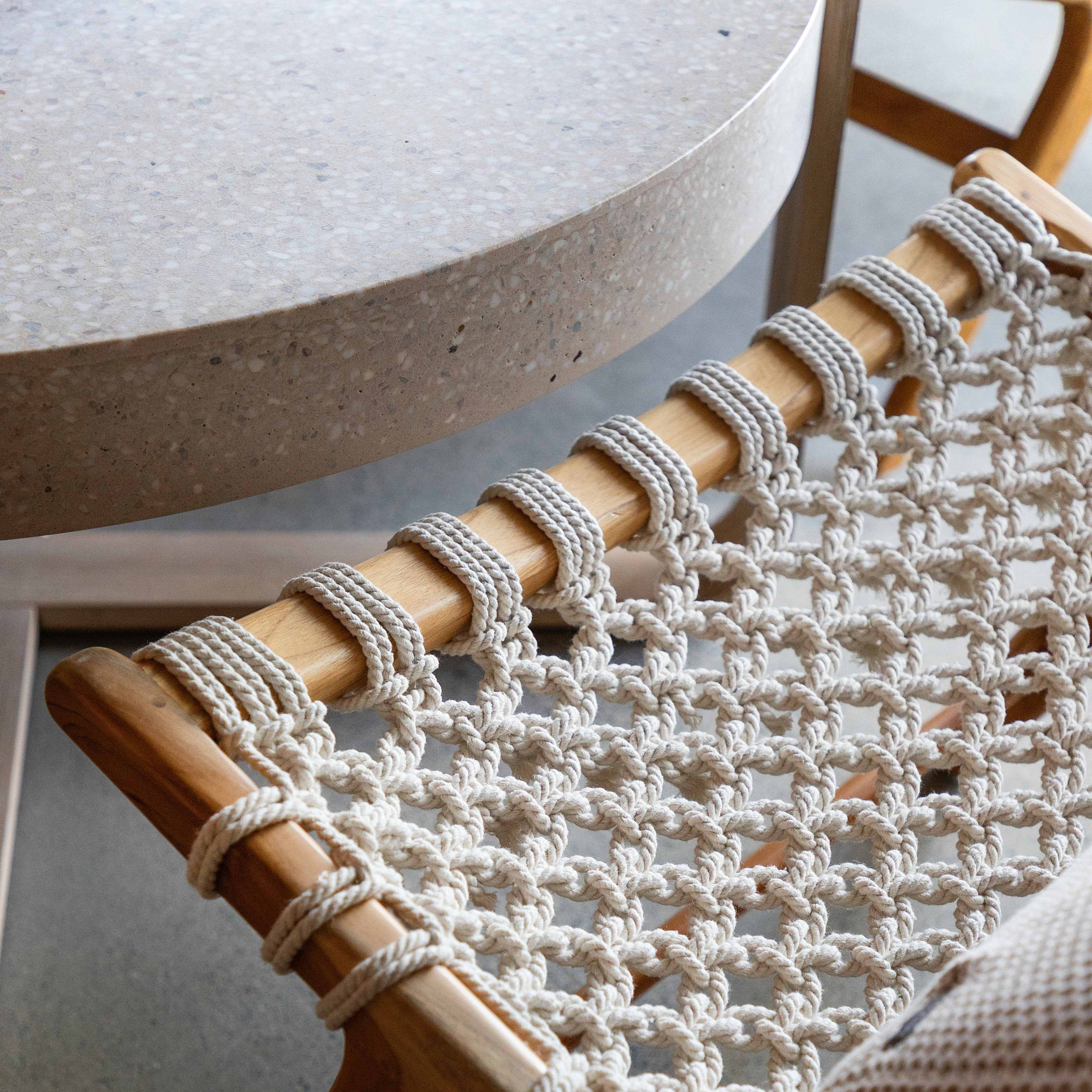 A close-up view of a woven chair seat made of natural fibers, resting beside a round, speckled concrete table.