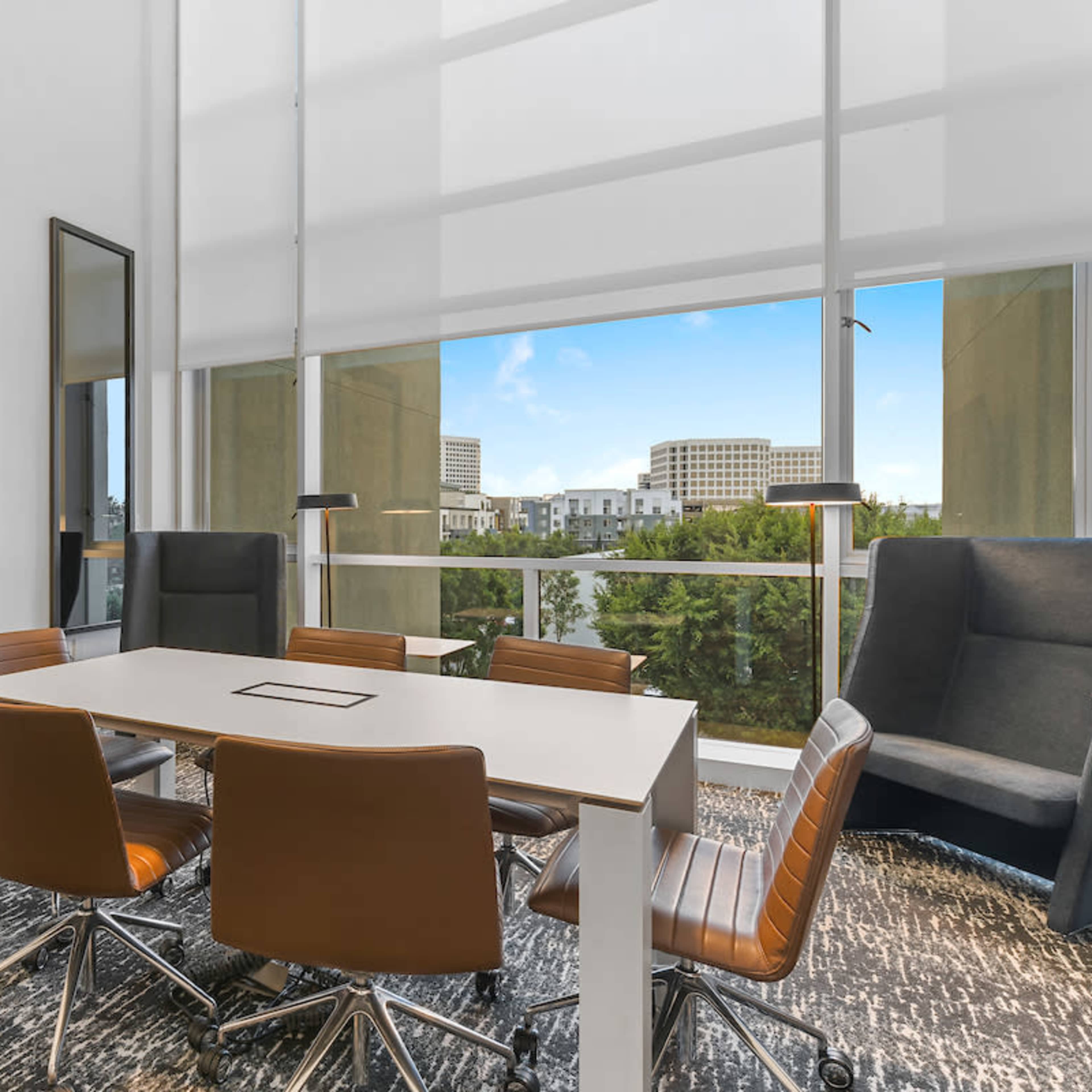 A modern conference room features a rectangular table surrounded by brown leather chairs and large windows overlooking a cityscape.