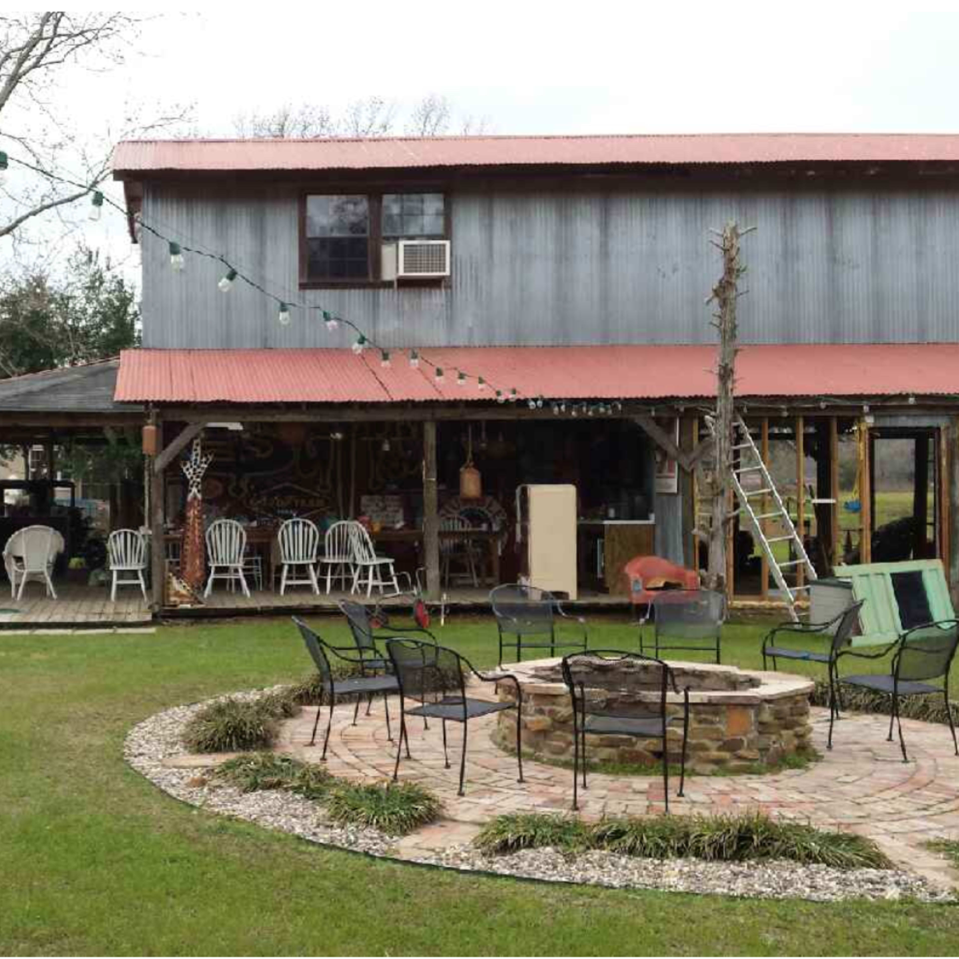 A two-story house with a red roof, surrounded by a grassy yard featuring a picnic table, fire pit, and decorated with string lights.