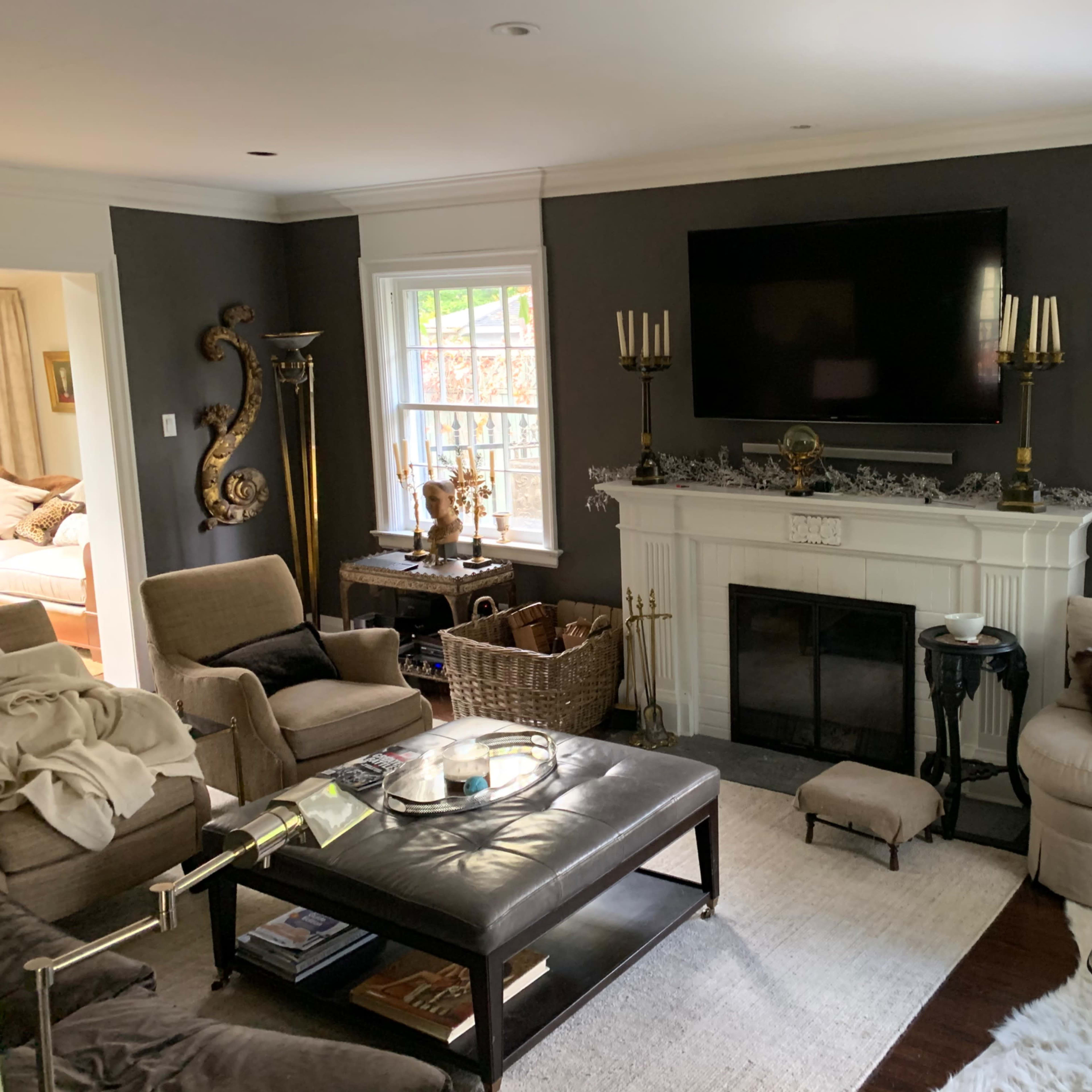 The living room features a dark accent wall, a large flat-screen TV above a white fireplace, and beige seating arranged around a coffee table.