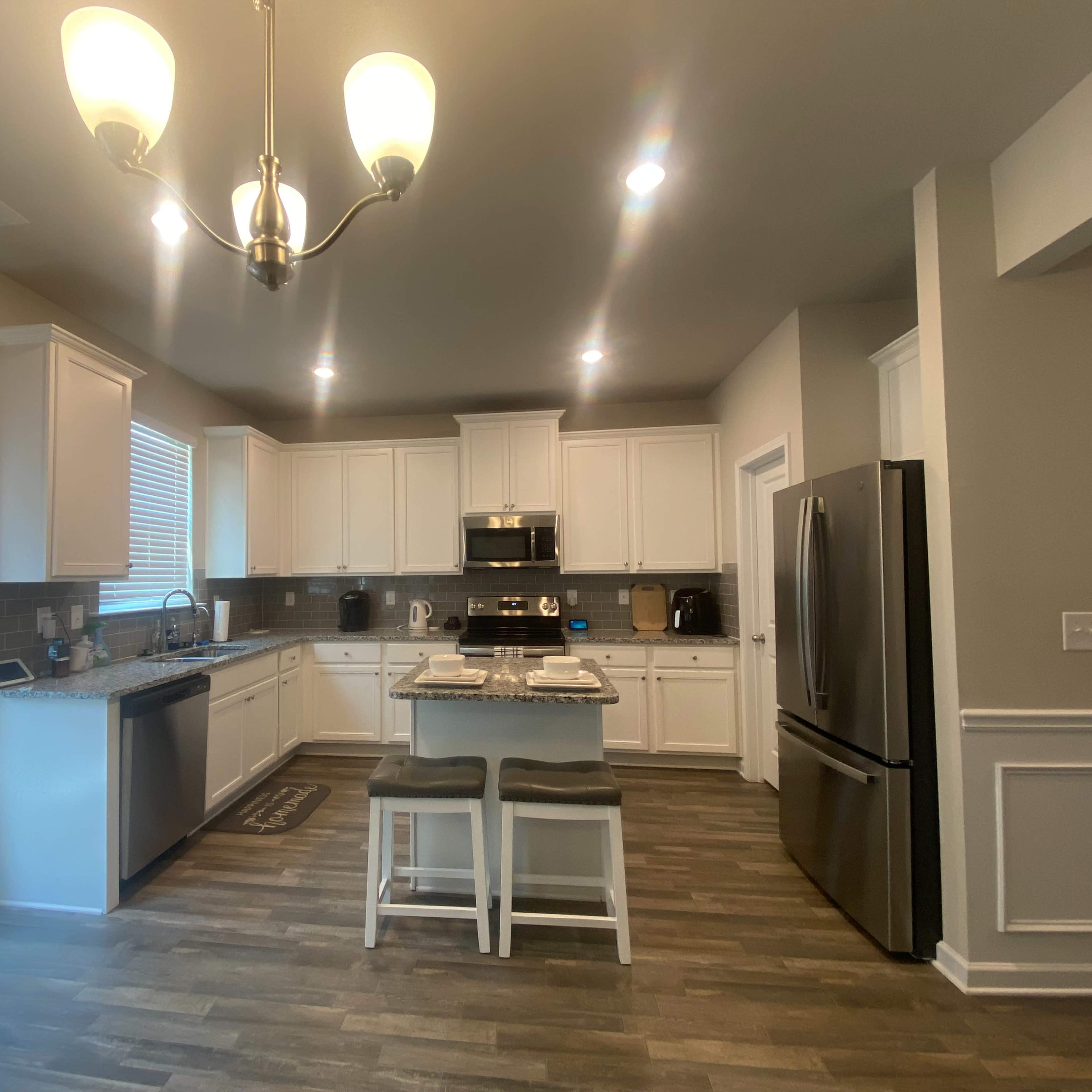 A modern kitchen with white cabinetry, granite countertops, stainless steel appliances, and a central island with two stools.