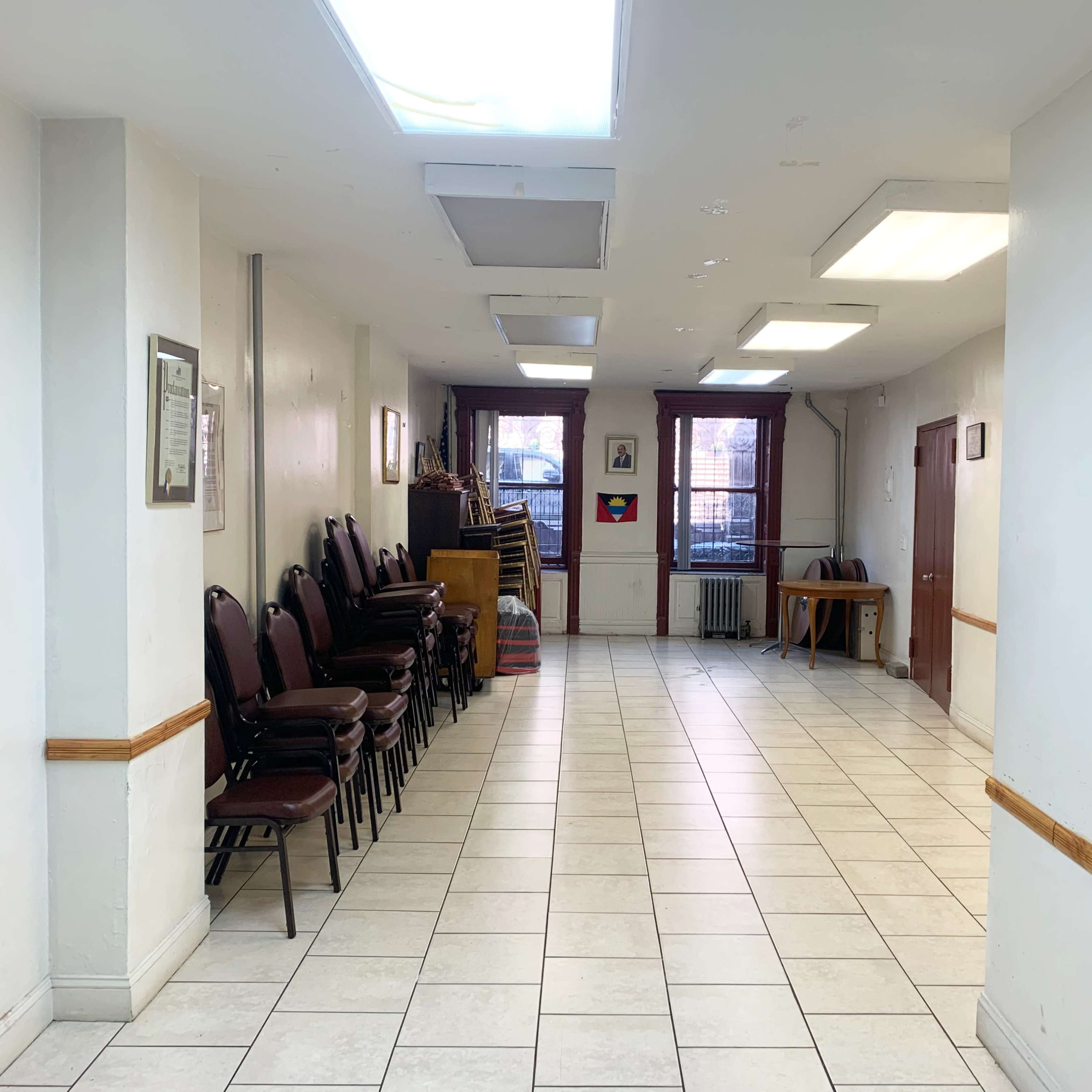 A long corridor with tiled floors, lined with stacked chairs on one side and windows at the far end.